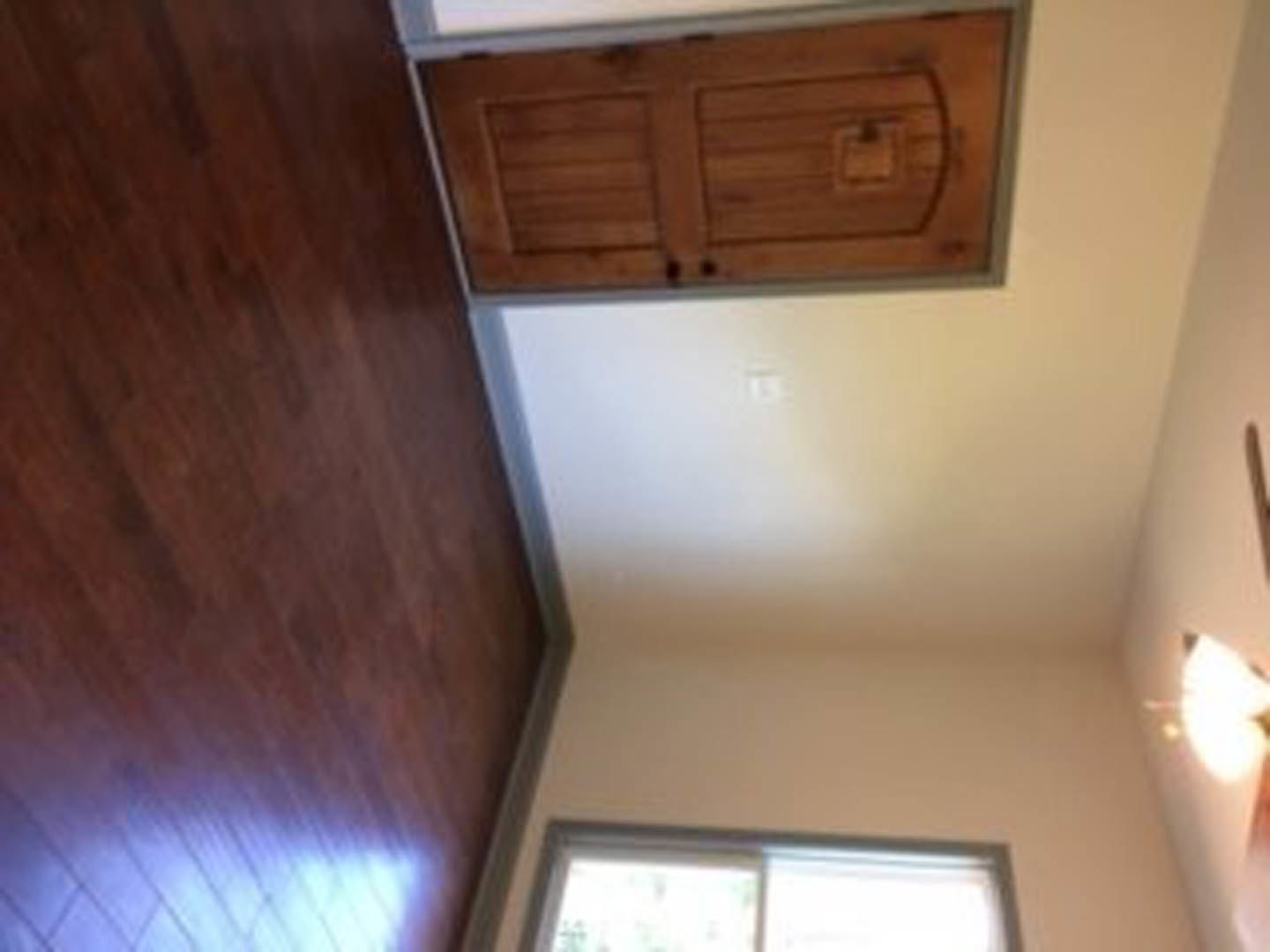 Room with light wood flooring, white walls, and a wooden door; window partially visible in background