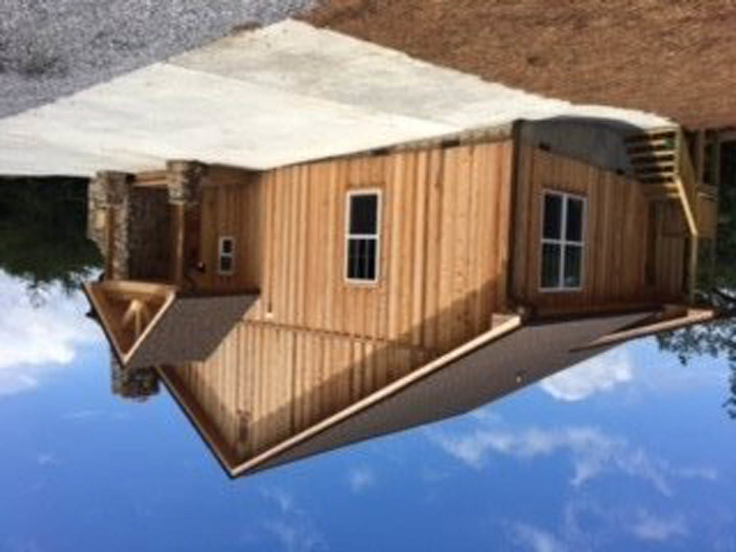 Wooden house exterior with prominent chimney, white-framed window, brown siding, and triangular roof peak against cloudy sky.