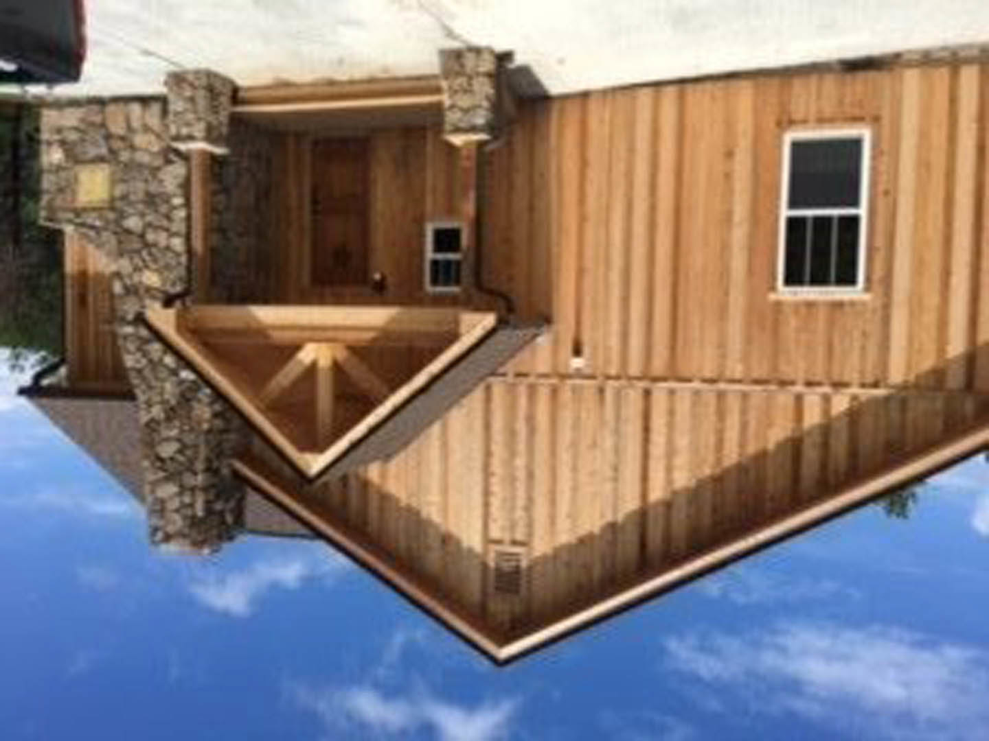 Stone roof atop a residential home, white-framed window, exposed wooden beam in corner, cloudy sky overhead