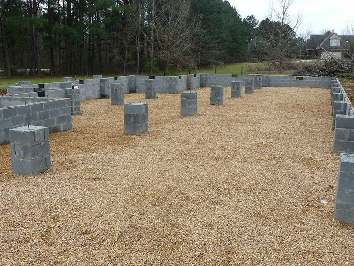 Concrete block foundation at residential construction site with exposed soil and scattered building materials