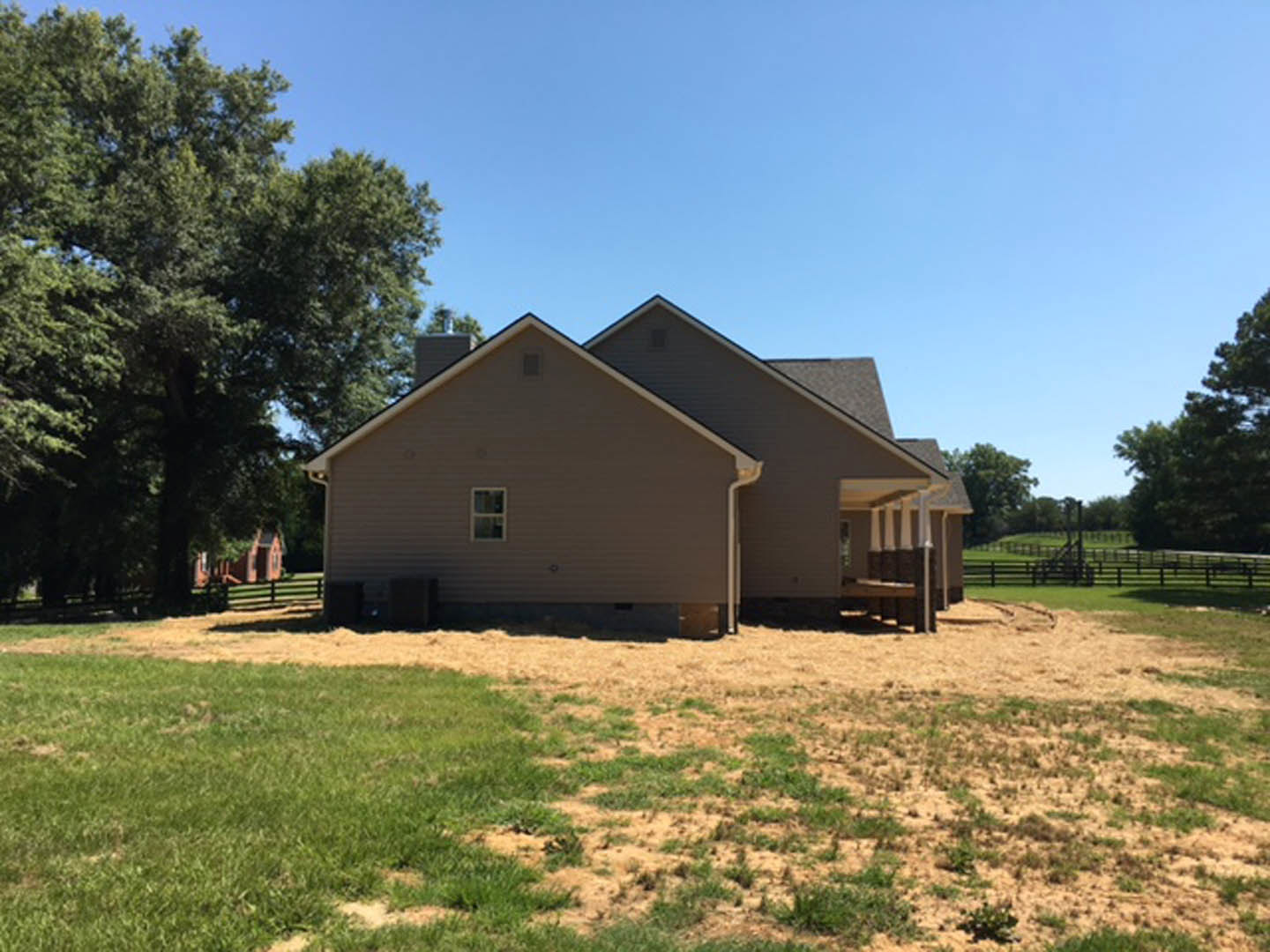 Two-story house with gabled roof, white siding, wooden fence, green lawn, and mature trees in the background