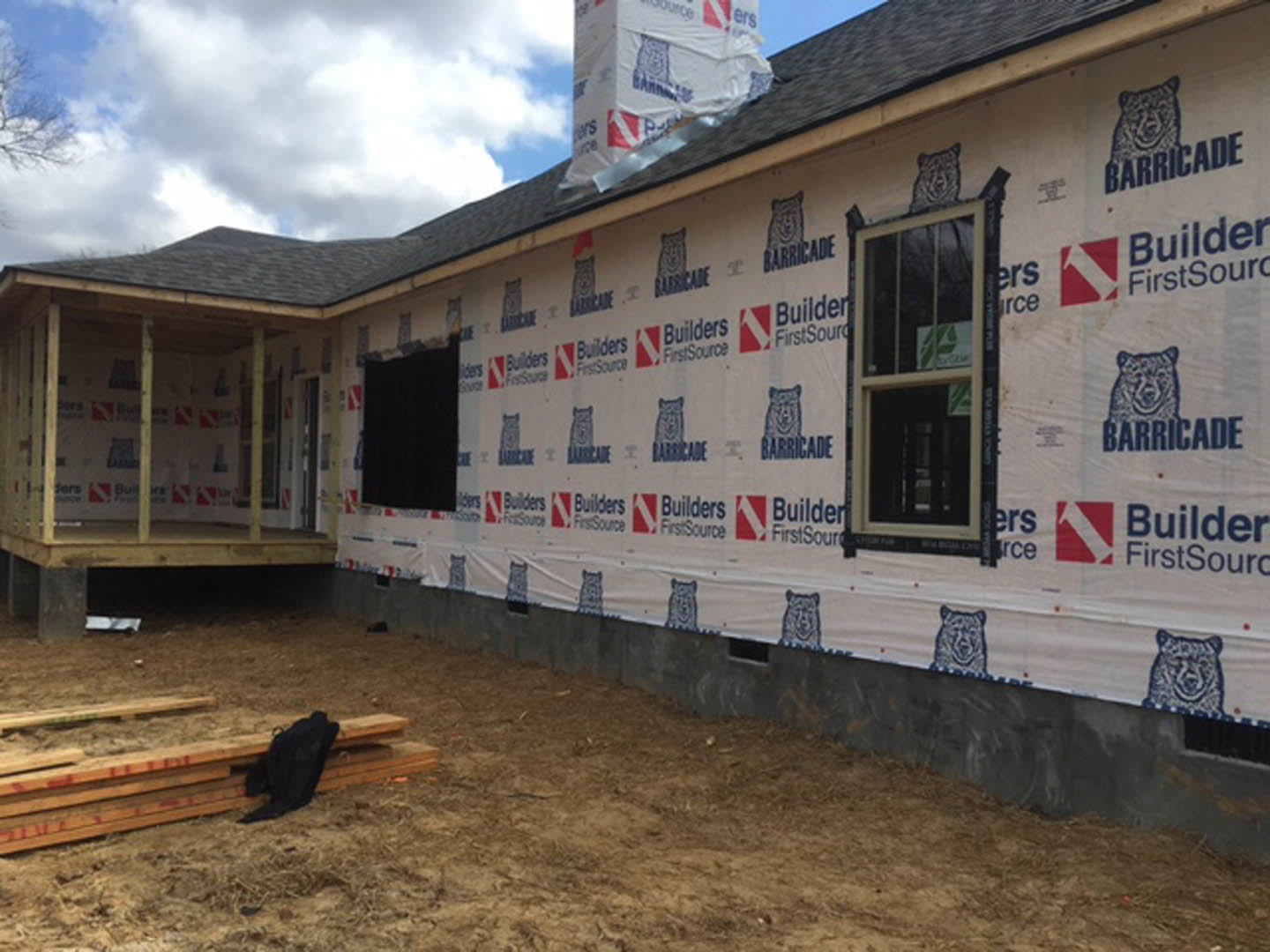 Partially built house with exposed wooden framing, scattered boards, unfinished deck and porch, person leaning on plank, window displaying sign, black animal on wood surface, white