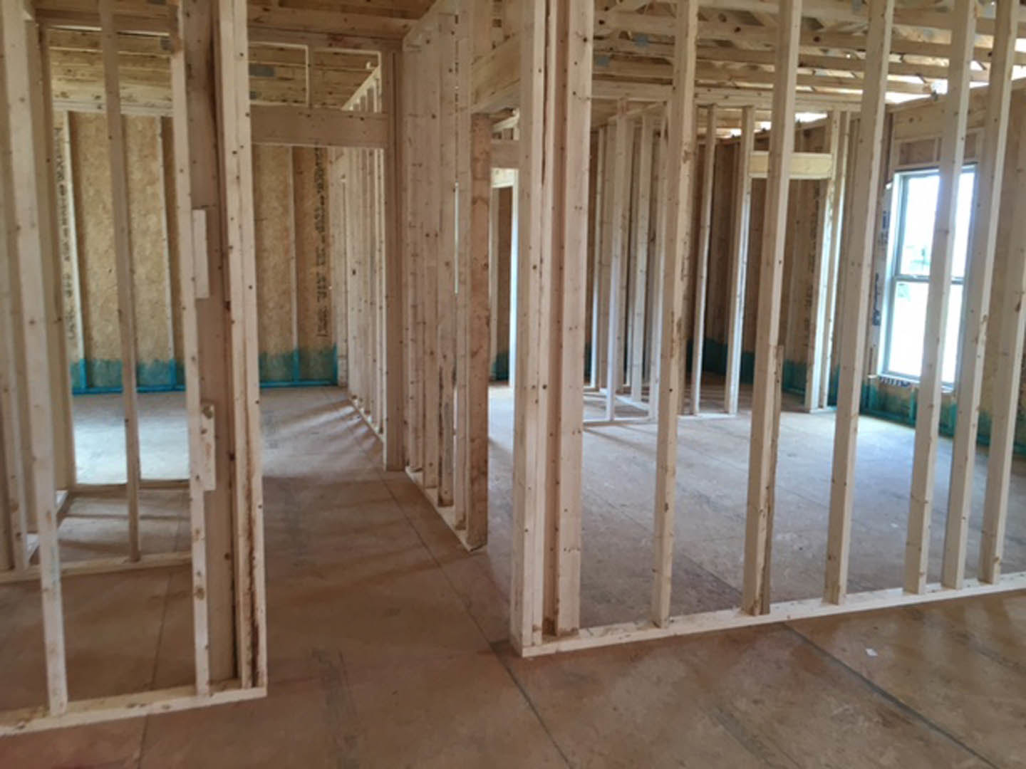 Wood-framed room with exposed beams, unfinished flooring, and a window set in a white frame against a blue wall