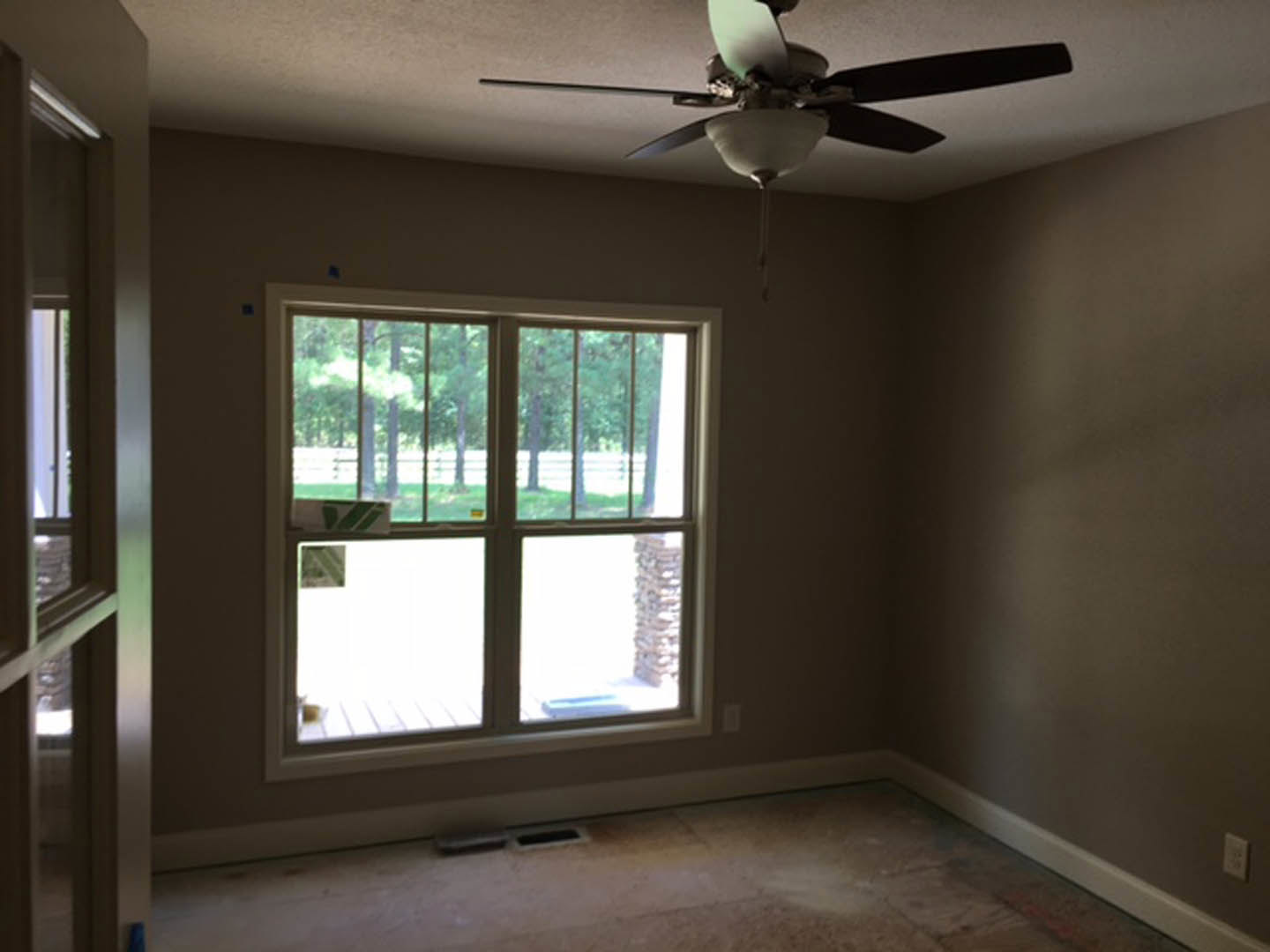 Ceiling fan with light fixture mounted on plaster ceiling above tile floor, window with trees visible outside