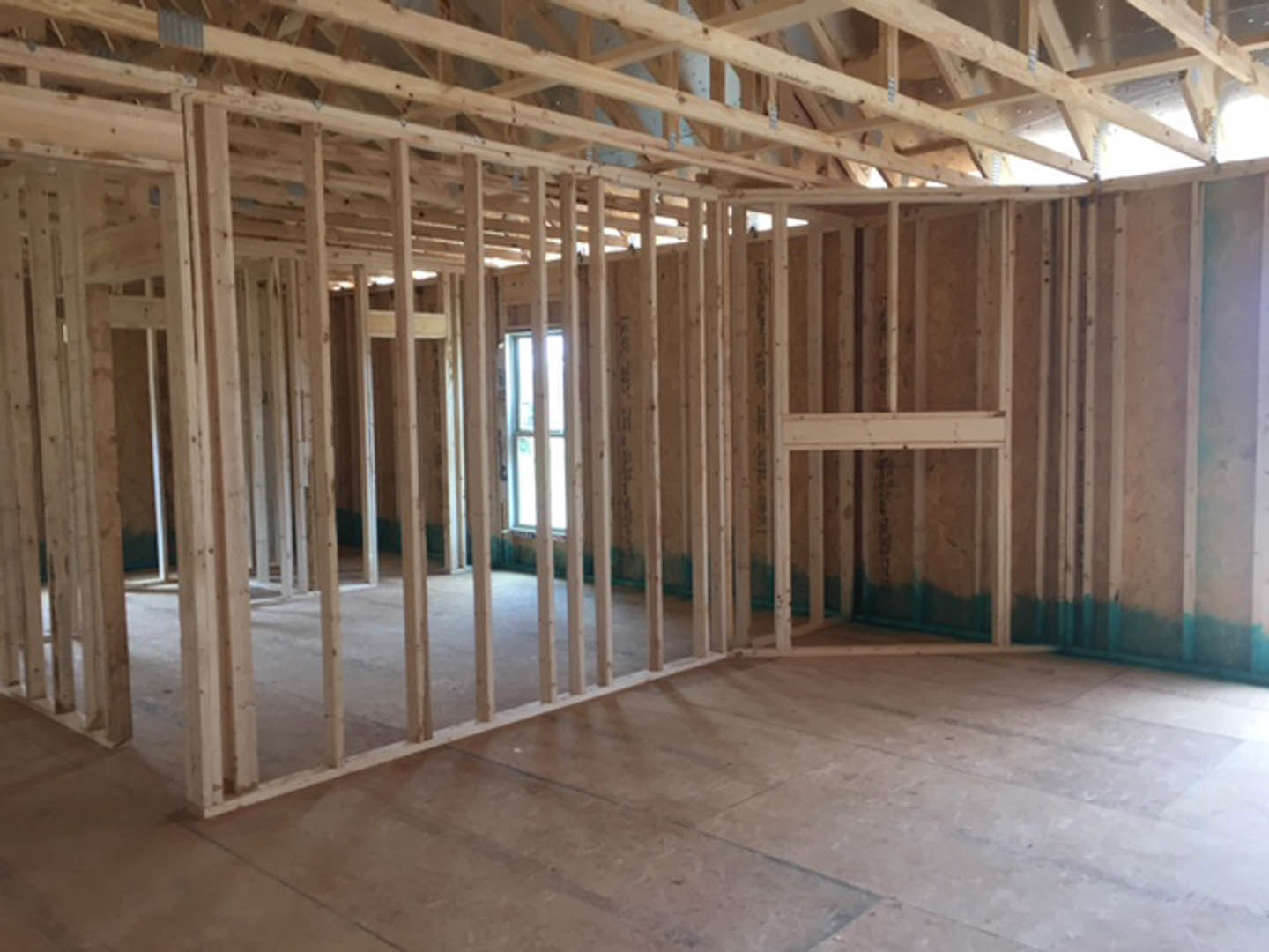 Wood-framed room with exposed beams, unfinished wooden floor, and white-framed window