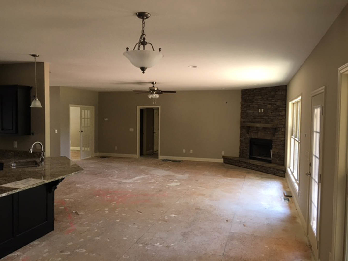 Living room with tile flooring, stone fireplace, ceiling fan, white plaster walls, and cabinetry visible in the background