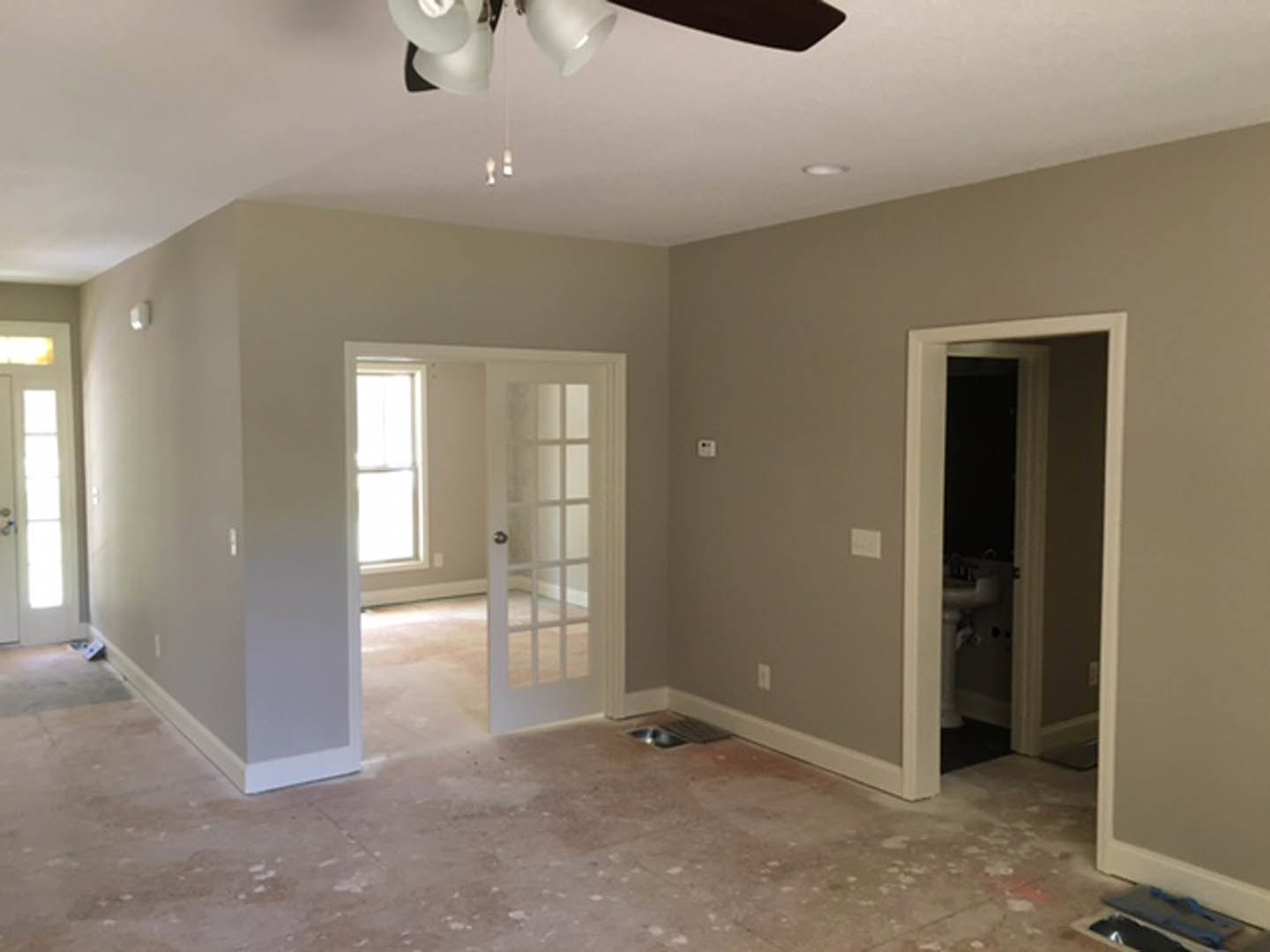 Neutral-toned room featuring a ceiling fan, paneled door with glass inserts, light-colored walls, and hardwood flooring
