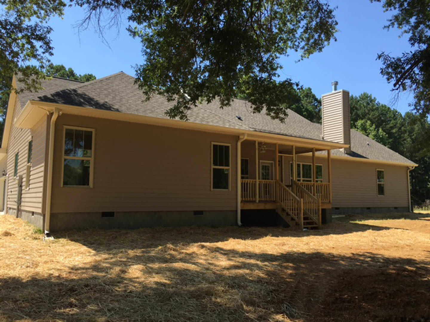 White siding house with covered porch, white railing, large front window, green lawn, mature tree in yard