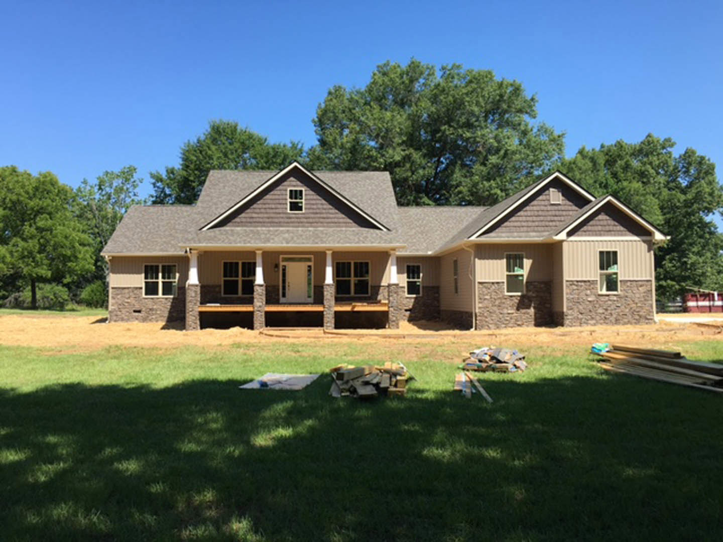 Two-story house with white siding, covered front porch, white door, green trim, grassy yard, stacked firewood, and mature trees.