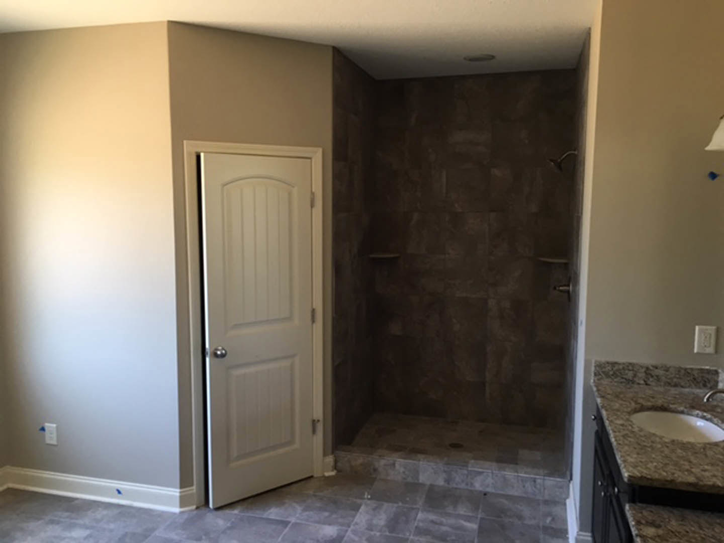 Modern bathroom featuring a glass-enclosed shower with gray tile walls, white porcelain sink with chrome faucet, light-colored plaster walls, and neutral tile flooring