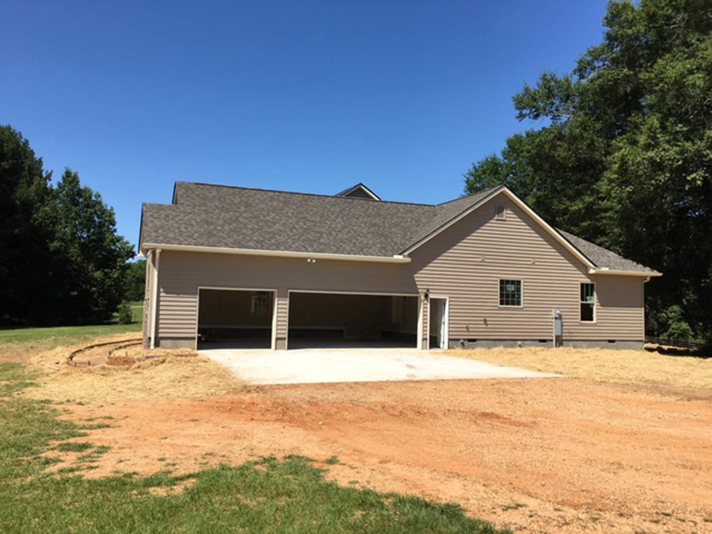 Two-story house with attached garage, light siding, shingle roof, manicured lawn, mature tree, and clear blue sky