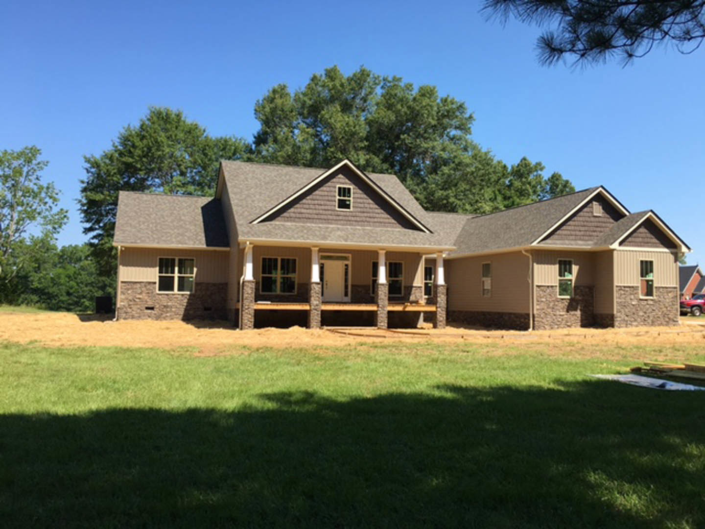Two-story house with covered porch, white front door, green lawn, and mature trees in the background