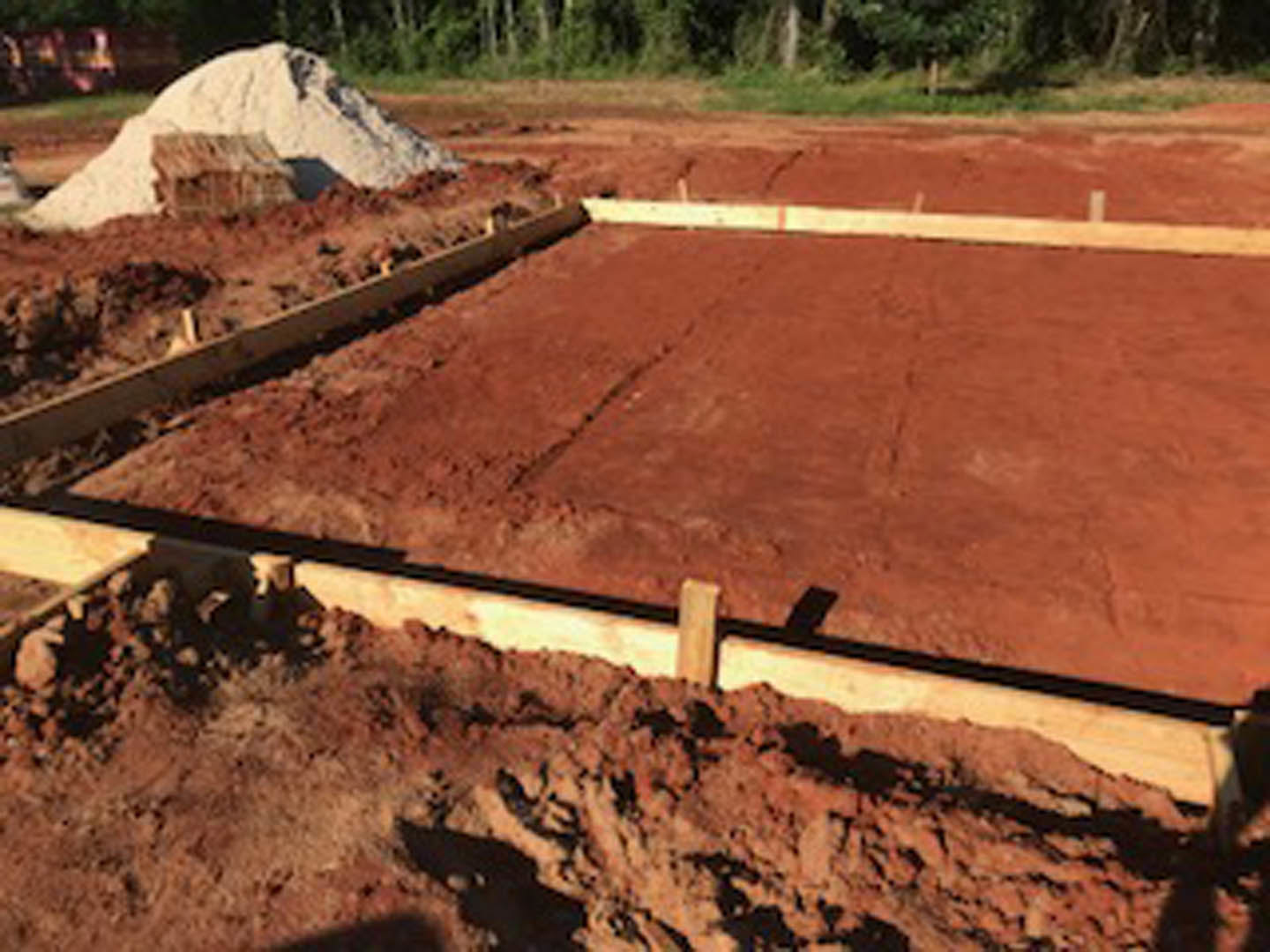 Wood beams forming the base of a home foundation surrounded by dirt, grass, and scattered rocks