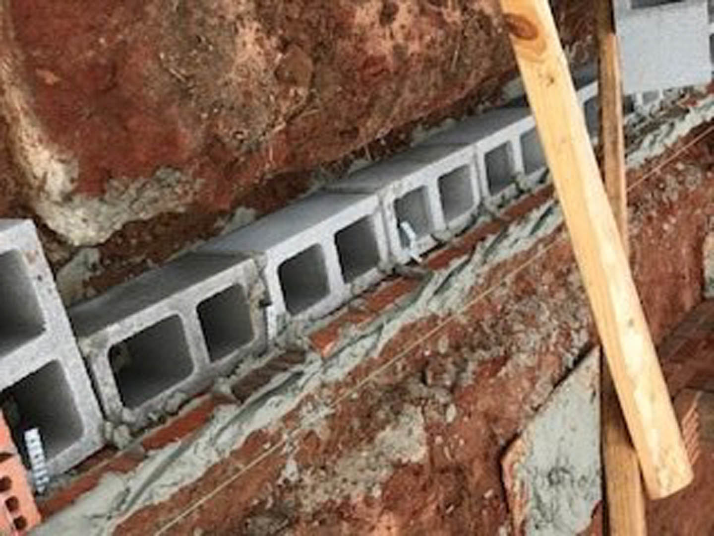 Stacked concrete blocks forming an exterior wall with visible mortar joints and a wooden beam attached above