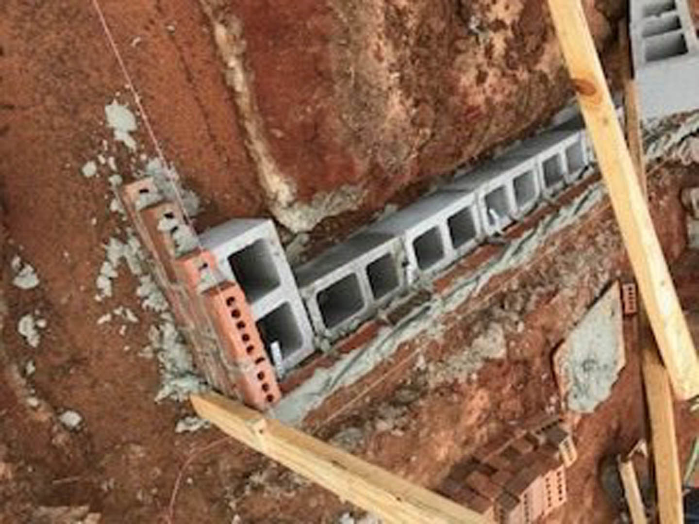Red brick exterior wall with evenly spaced holes above a concrete foundation, outdoor residential setting
