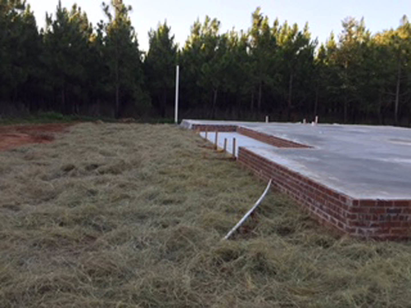 Red brick exterior home with manicured lawn, mature trees in the background, and clear sky above