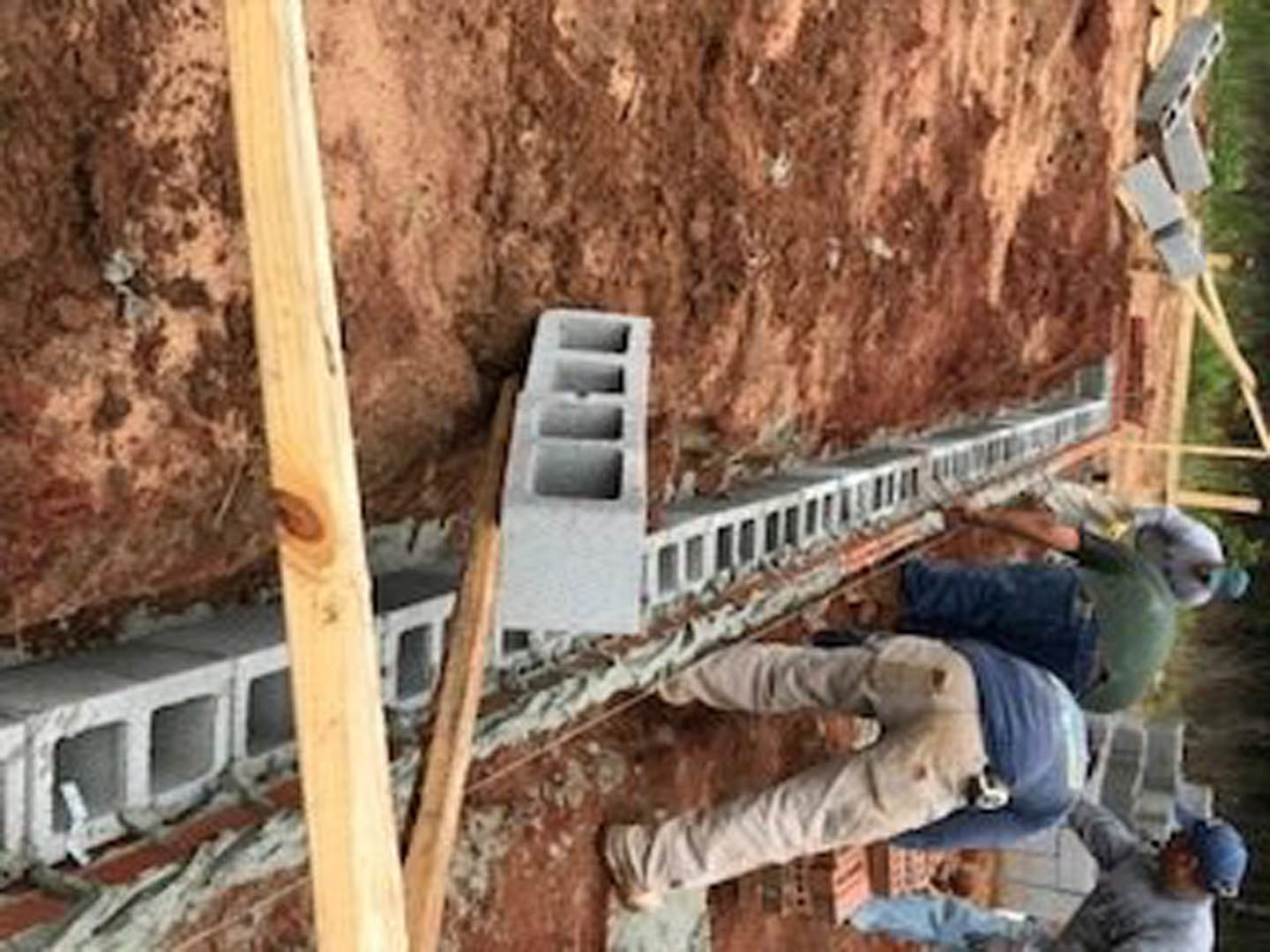 Workers in hard hats and vests assemble framing and exterior walls on a custom home construction site with exposed wood beams and unfinished surfaces.
