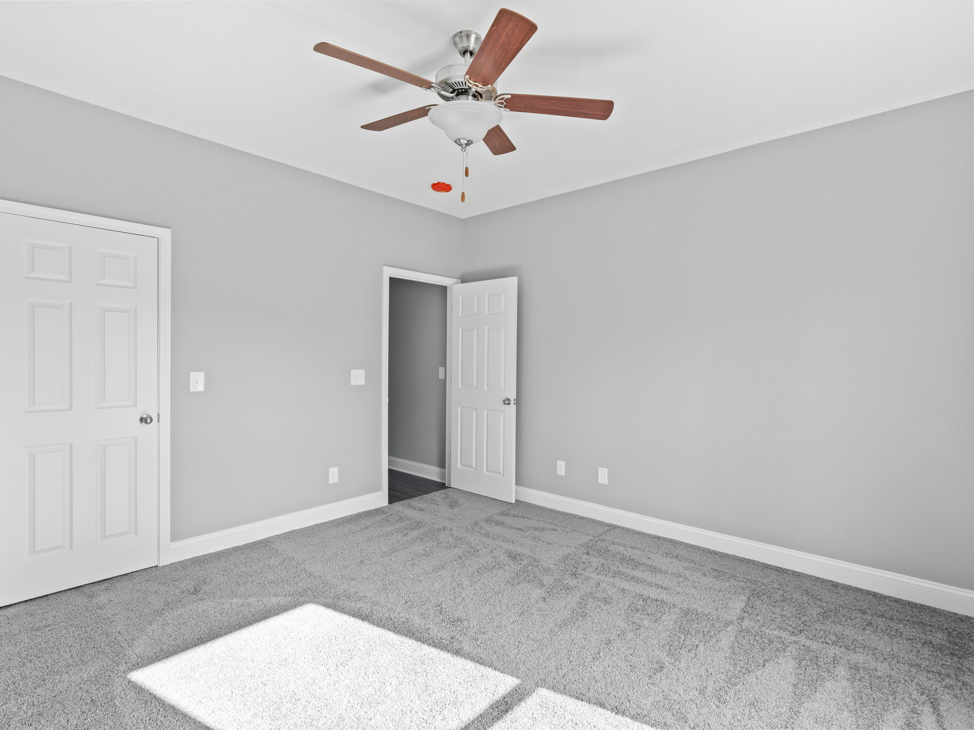 Ceiling fan with light fixture mounted on white ceiling above neutral-toned room, white paneled door with silver knob, plaster walls, and light flooring