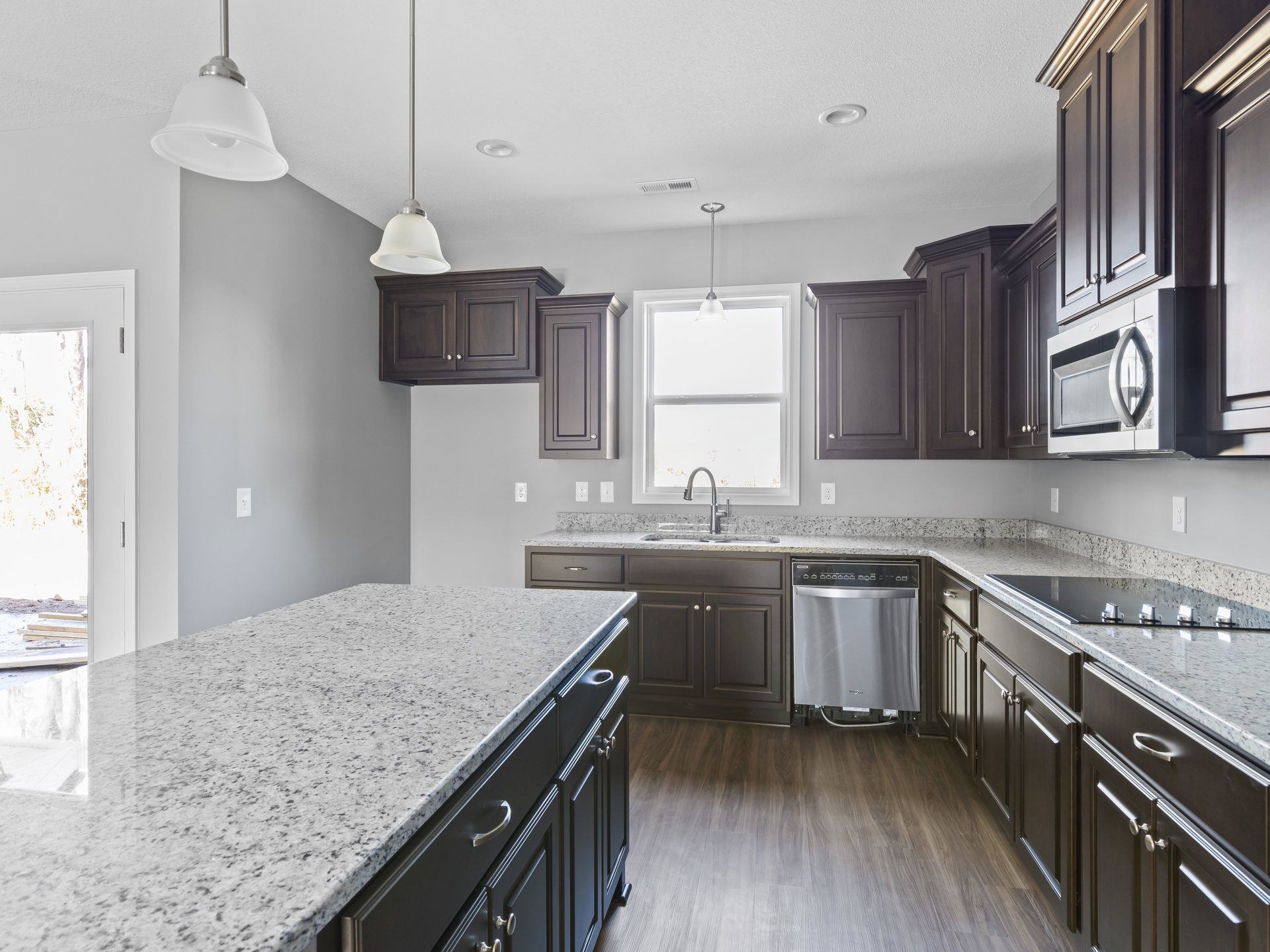 Granite countertops, stainless steel dishwasher, white sink beneath window, black drawer cabinetry, chrome faucet, built-in microwave oven