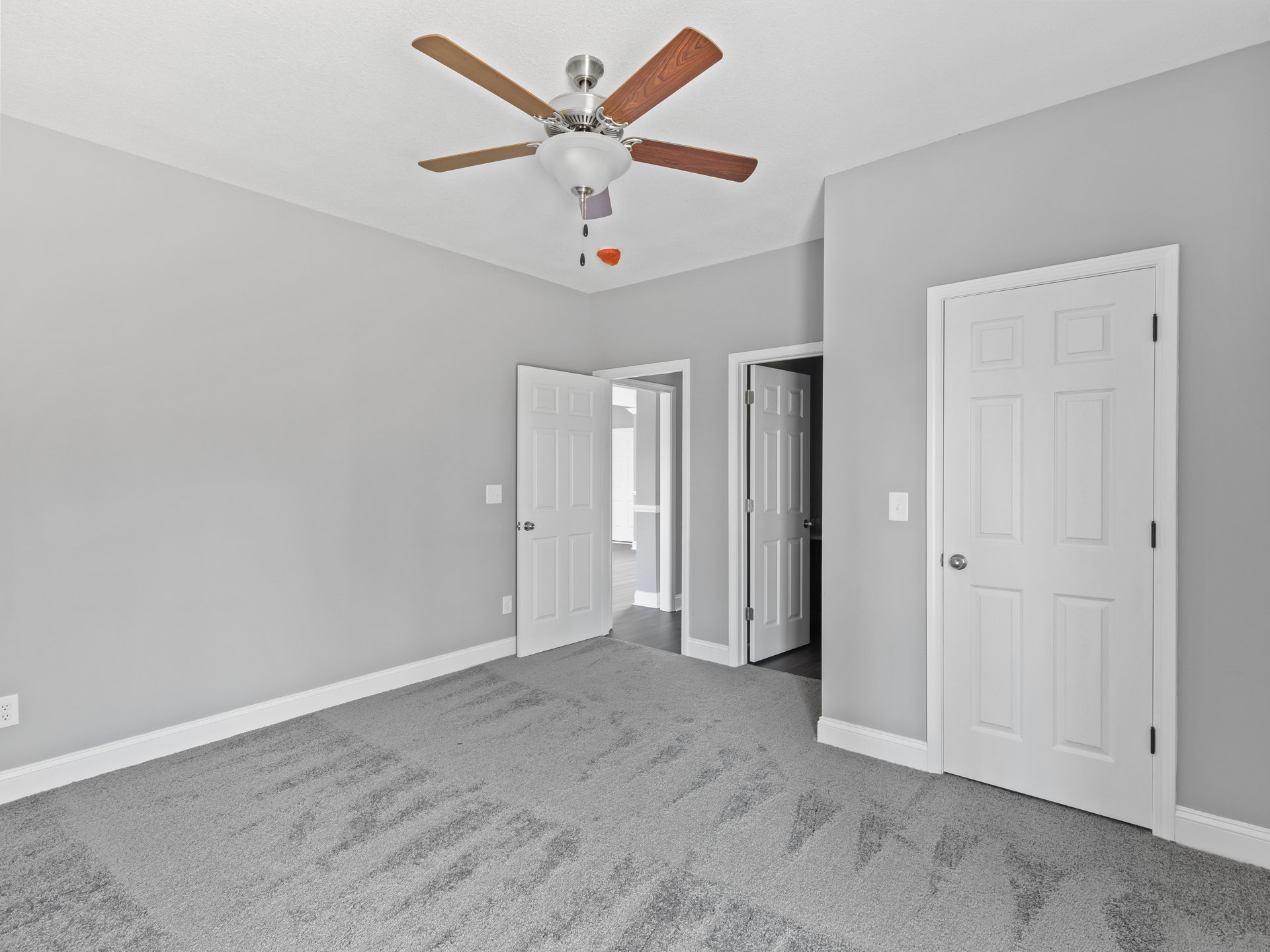 Carpeted room with a ceiling fan and light fixture, two white doors with silver knobs, neutral walls, and plaster ceiling