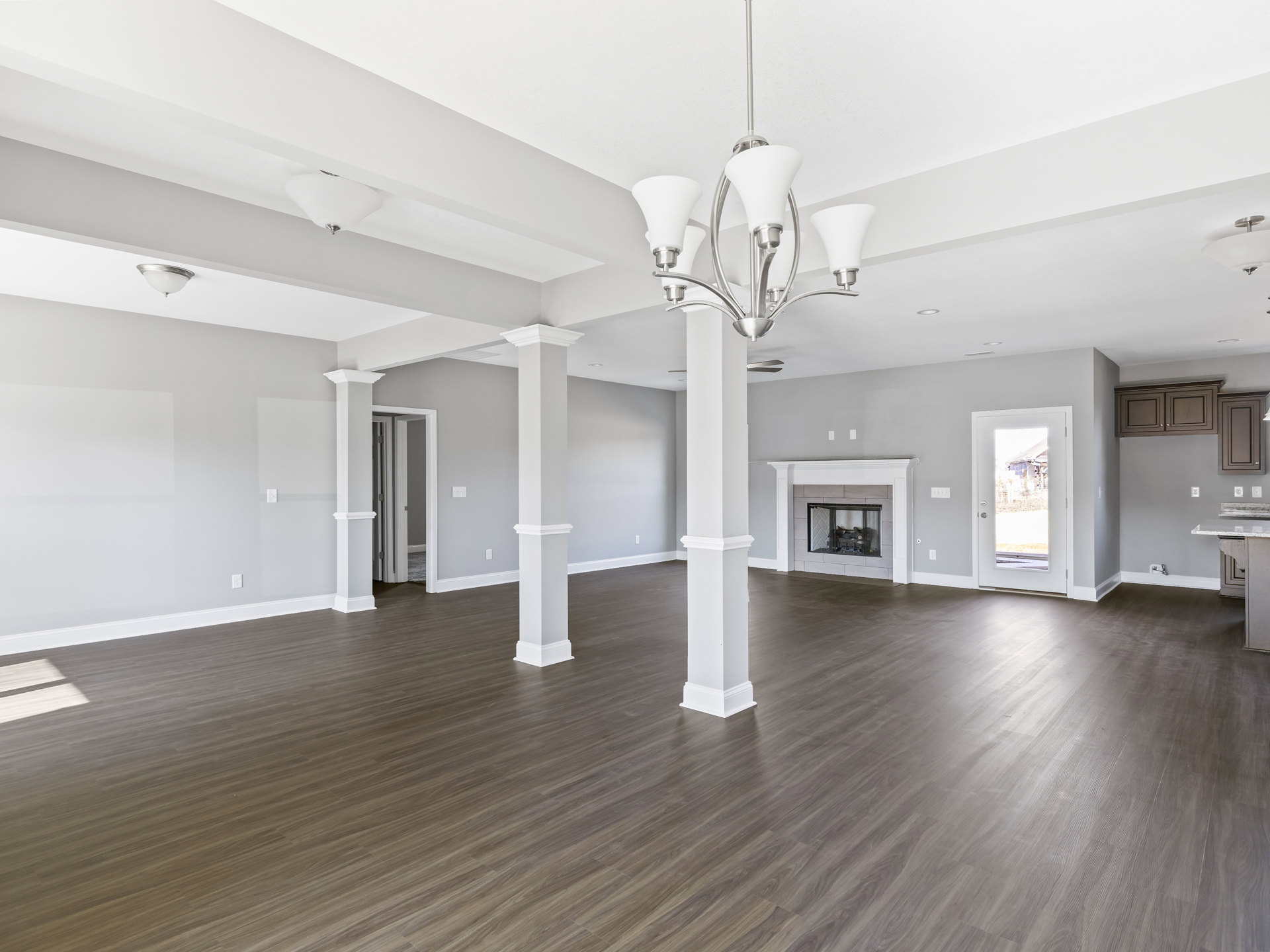 Spacious living area featuring white pillars, wood flooring, plaster walls, ceiling fixtures, and a glass-door fireplace