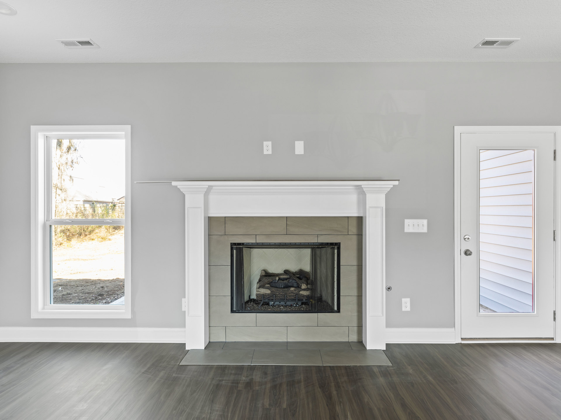 Stone fireplace with log and rocks, tile flooring, white door with window, window view of fence and neighboring house