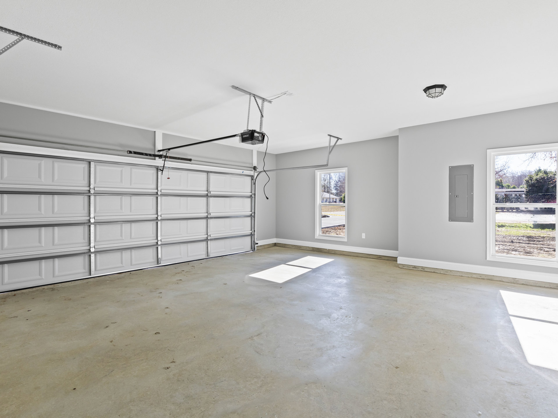 Garage interior with white tile flooring, plaster walls, ceiling-mounted light fixture, and a garage door featuring a handle; white surfaces cast shadows on concrete.