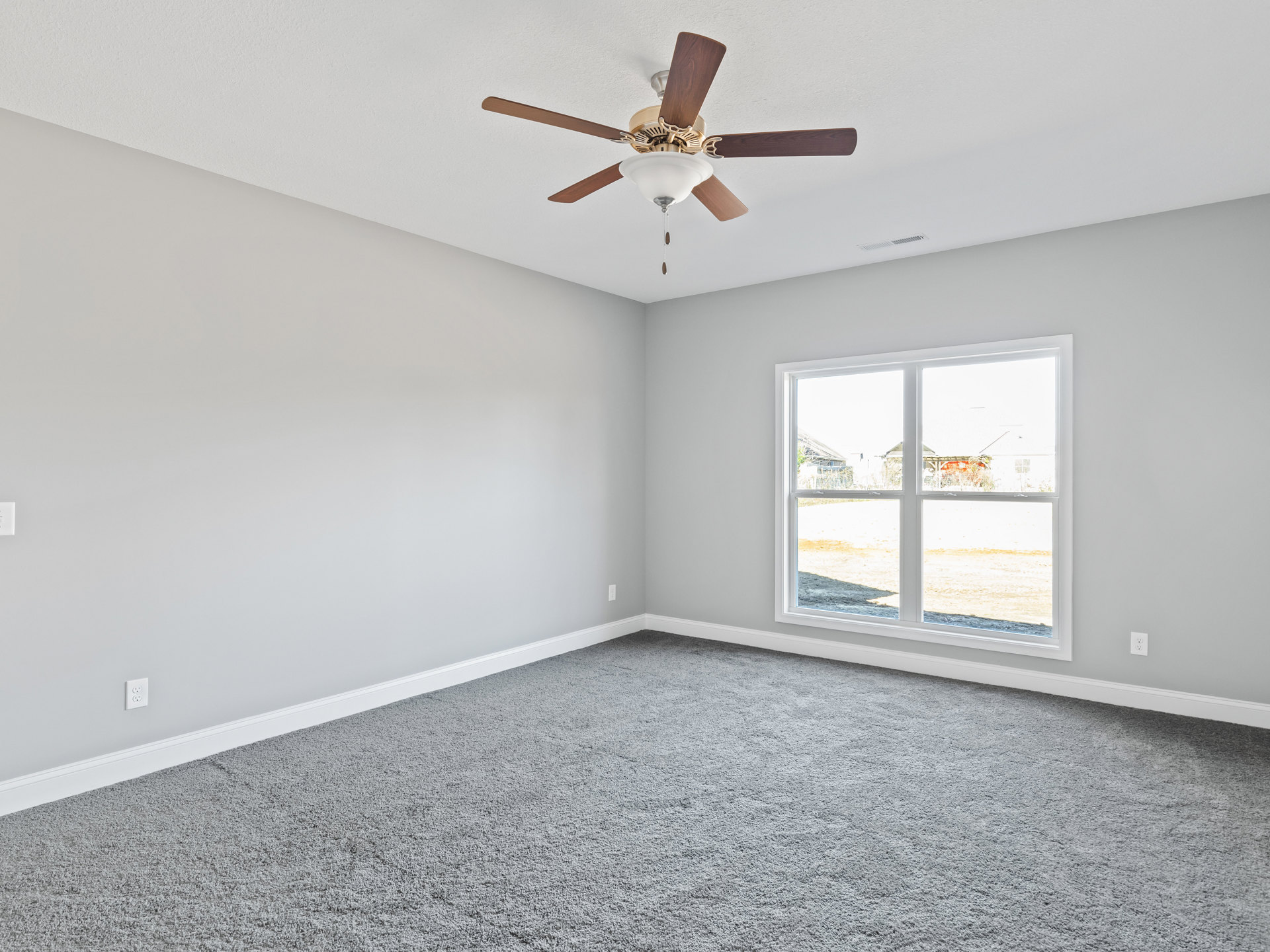 Bedroom with grey carpet, white walls, ceiling fan with light fixture, large window overlooking green yard