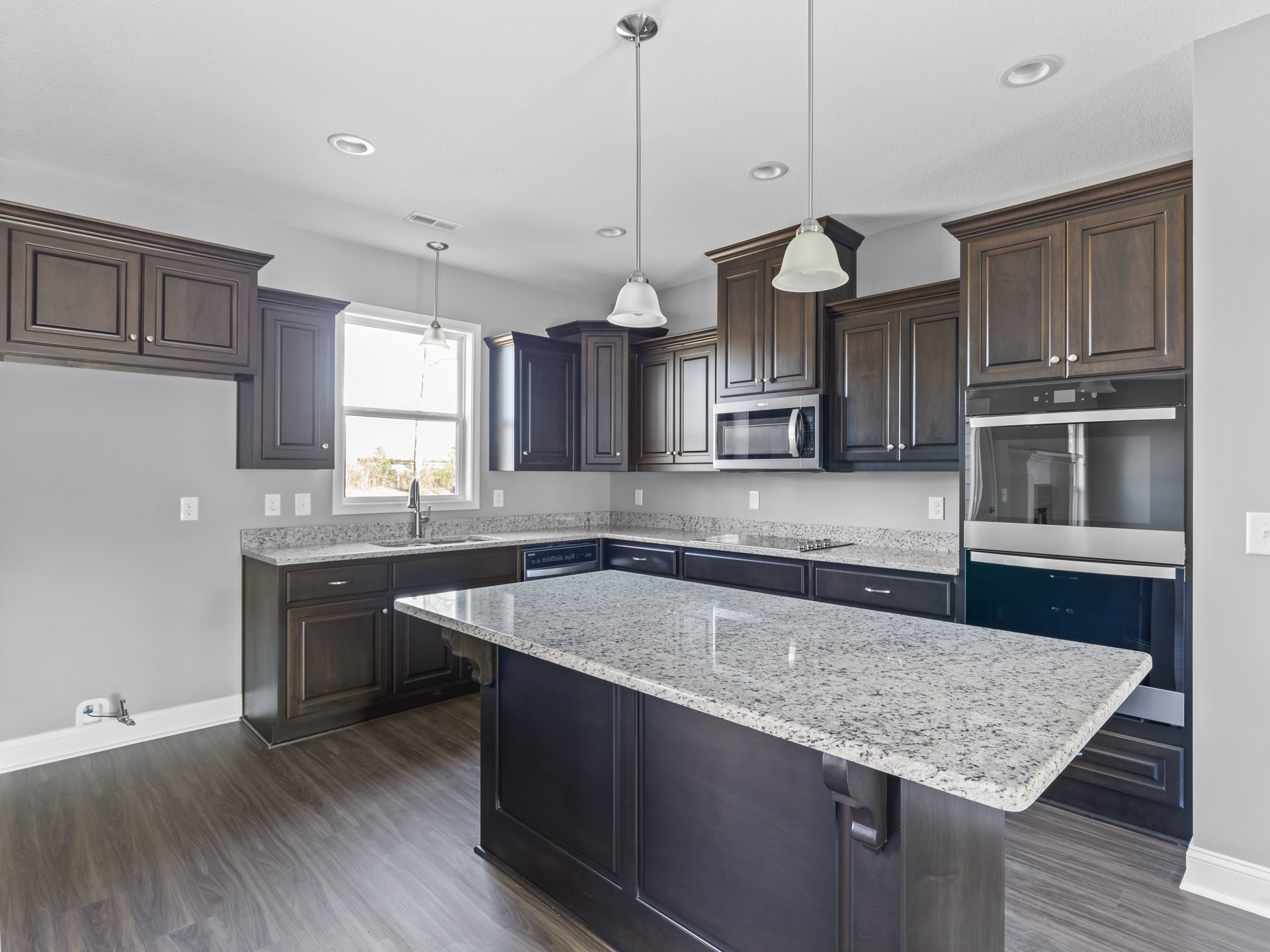 Kitchen with dark wood cabinets, marble island countertop, stainless steel microwave, ceiling light fixture, sunlight streaming through window, and modern sink.