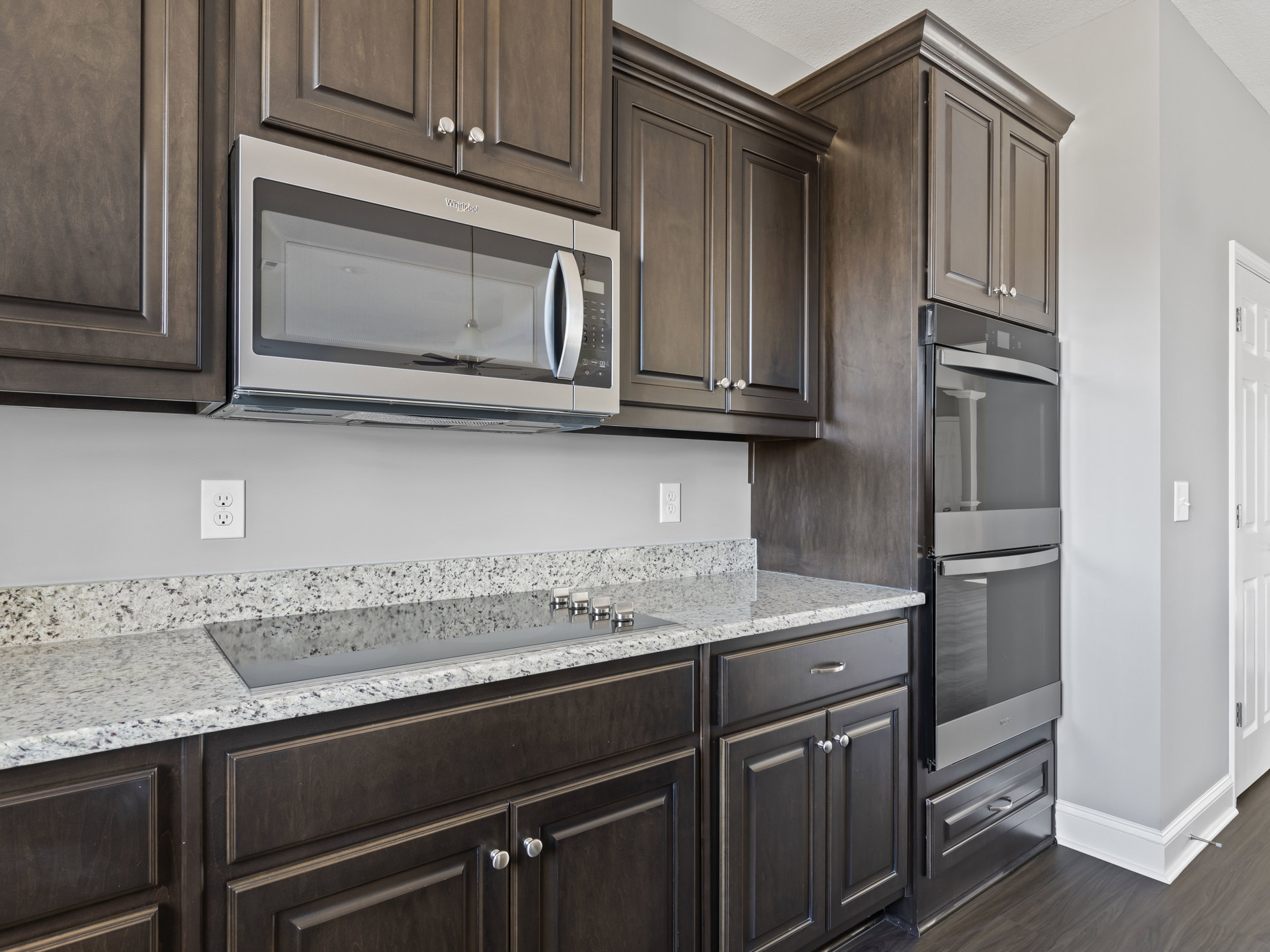 Dark wood kitchen cabinets, stainless microwave with vent hood, granite countertops, white electrical outlet, stainless refrigerator, cabinet drawers and doors