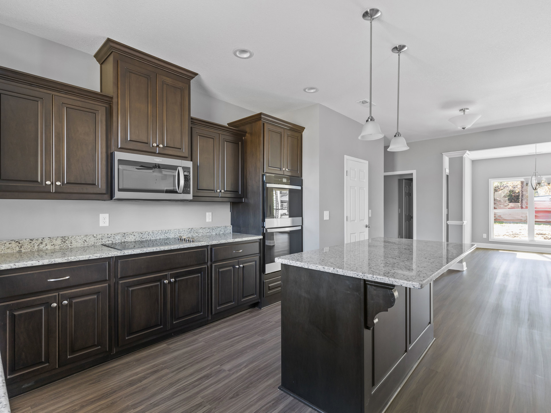Marble kitchen island with waterfall edge, dark wood cabinets, stainless steel microwave with vent hood, pendant lighting, and light hardwood flooring