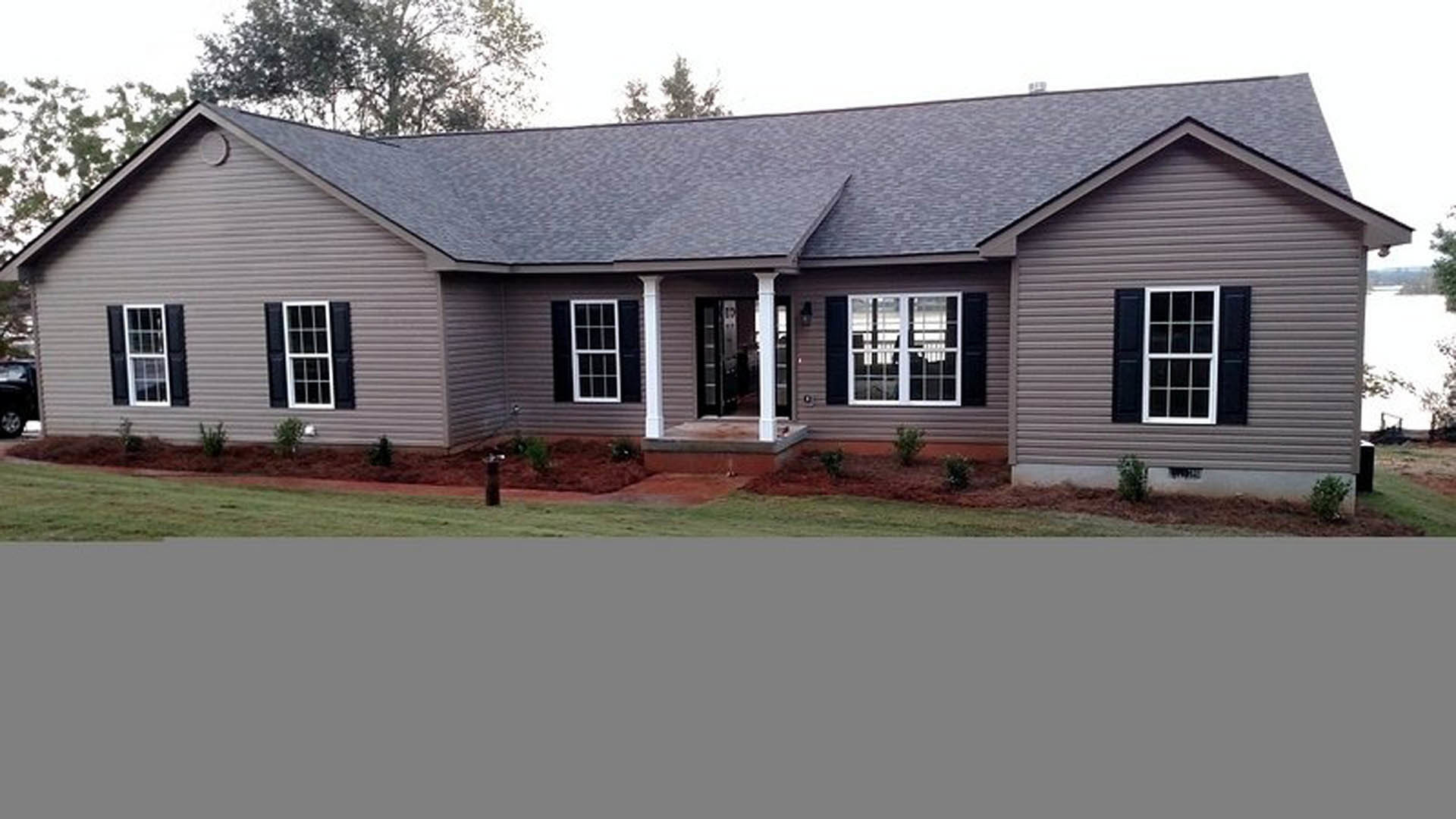 Two-story farmhouse with white siding, dark roof, large windows with white frames, and a manicured green lawn in front
