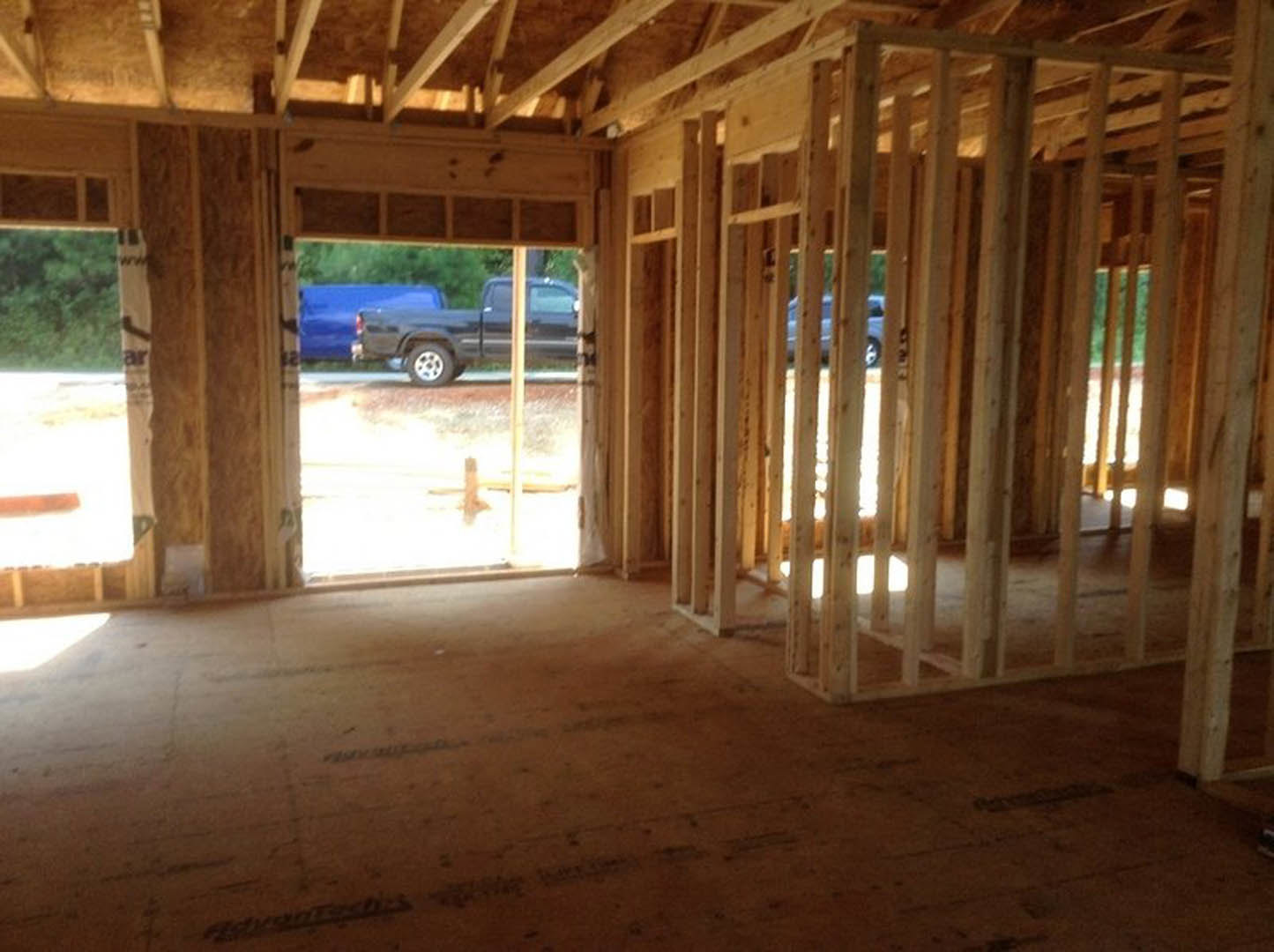 Exposed wood framing and beams in an unfinished room with plywood flooring and large windows