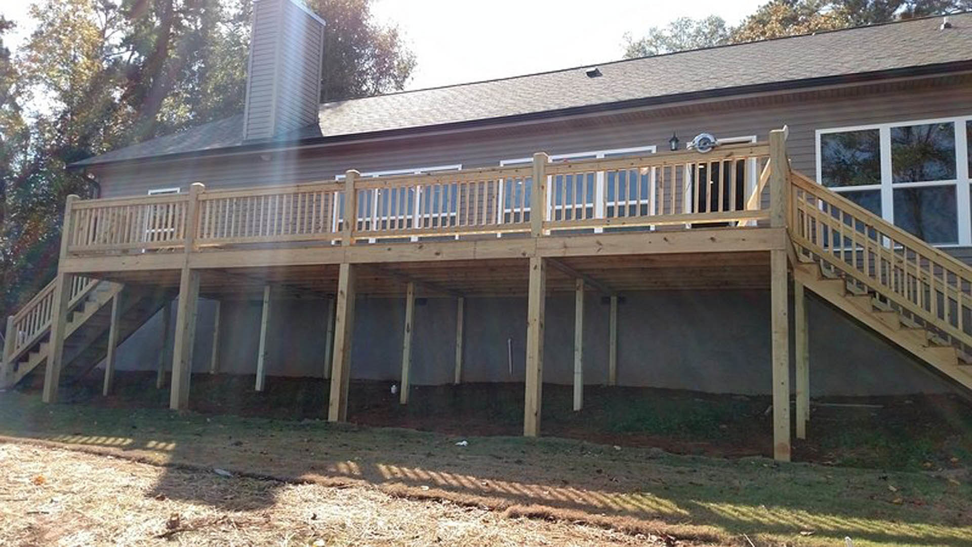 Wood deck with railing attached to white siding home, outdoor staircase leading to yard, large windows, tree branches visible, sunlight casting bird-shaped shadow on ground