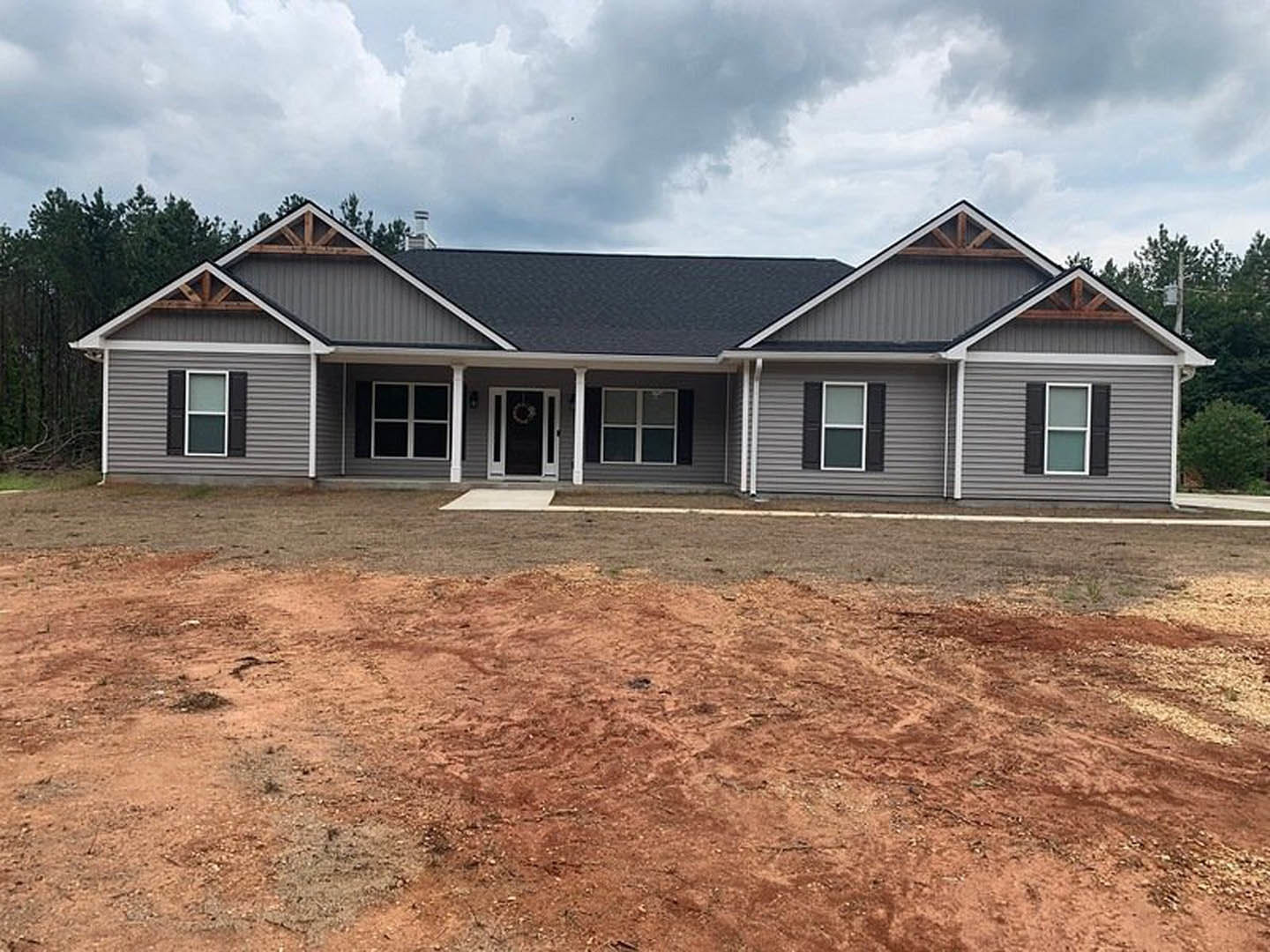 Modern house with black roof, white-framed windows, black and white front door, dirt yard in foreground, cloudy sky overhead