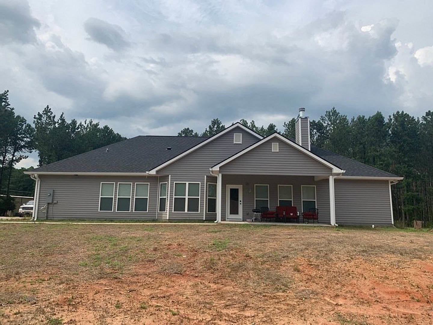 Two-story house with white siding, covered front porch, large windows, green lawn, mature trees in background, and cloudy sky overhead