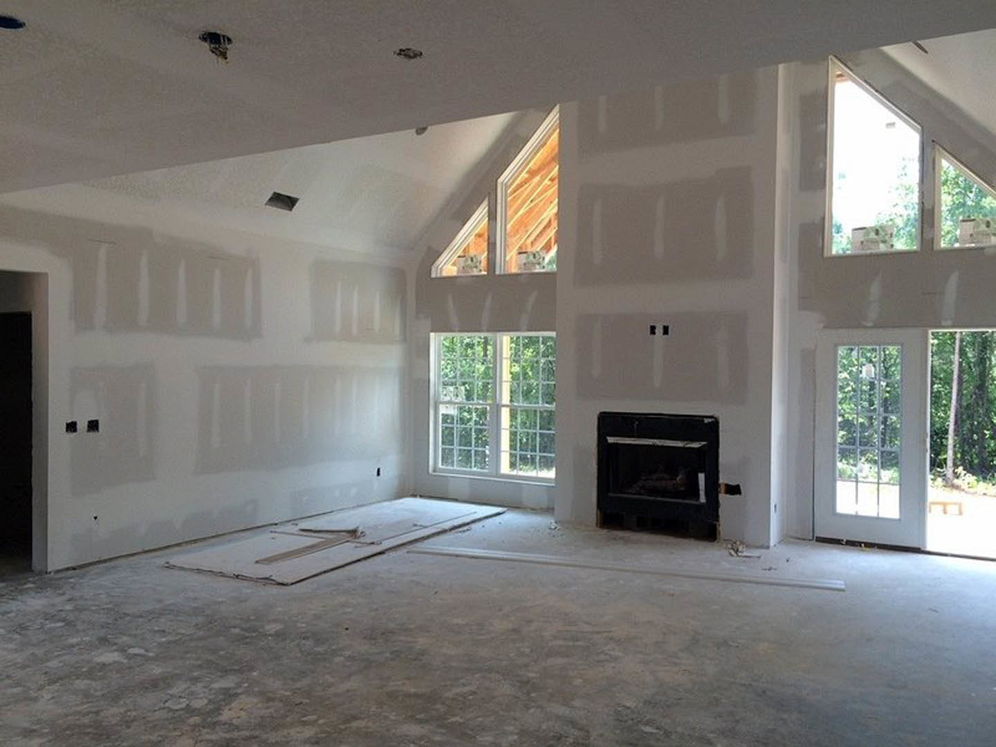 Living room with concrete floors, large grid windows, modern fireplace set in a white wall, and exposed ceiling beams