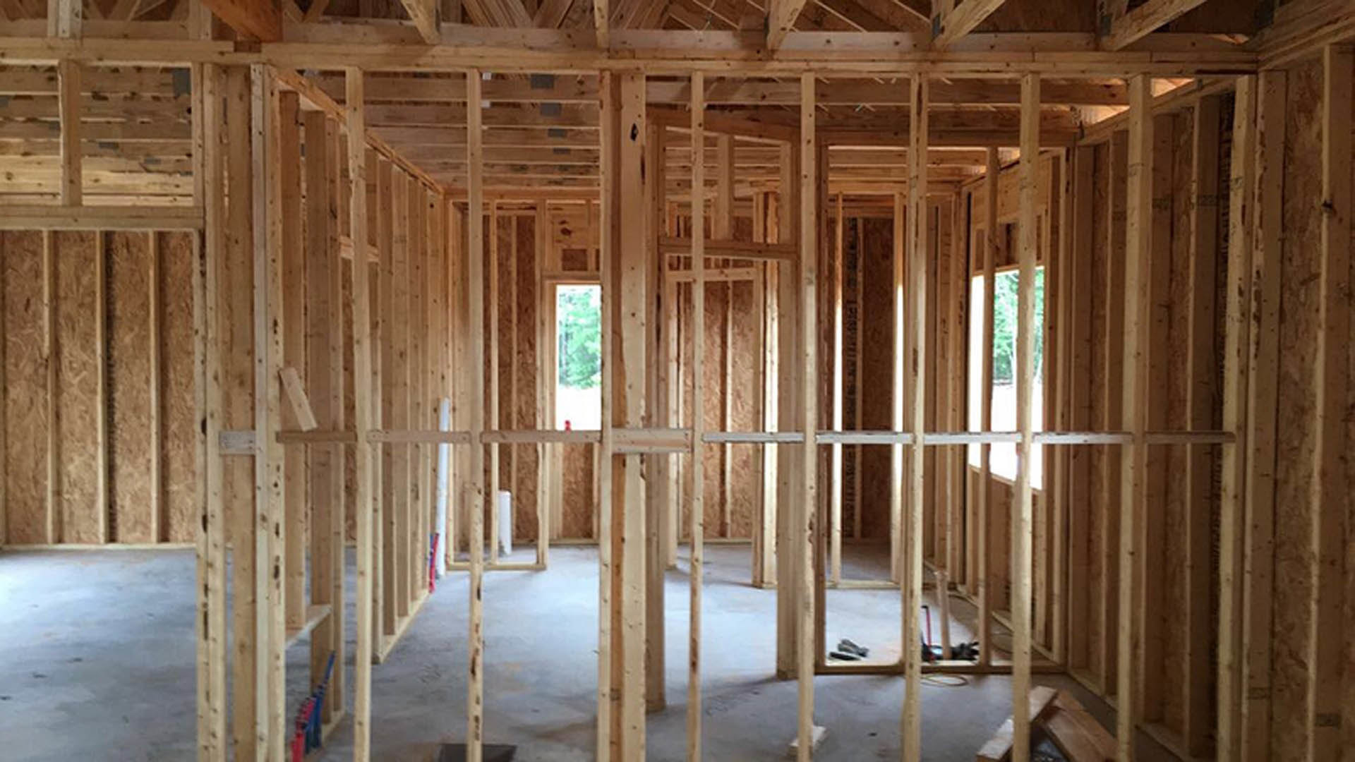 Wood-framed interior under construction with exposed beams, unfinished walls, and visible lumber