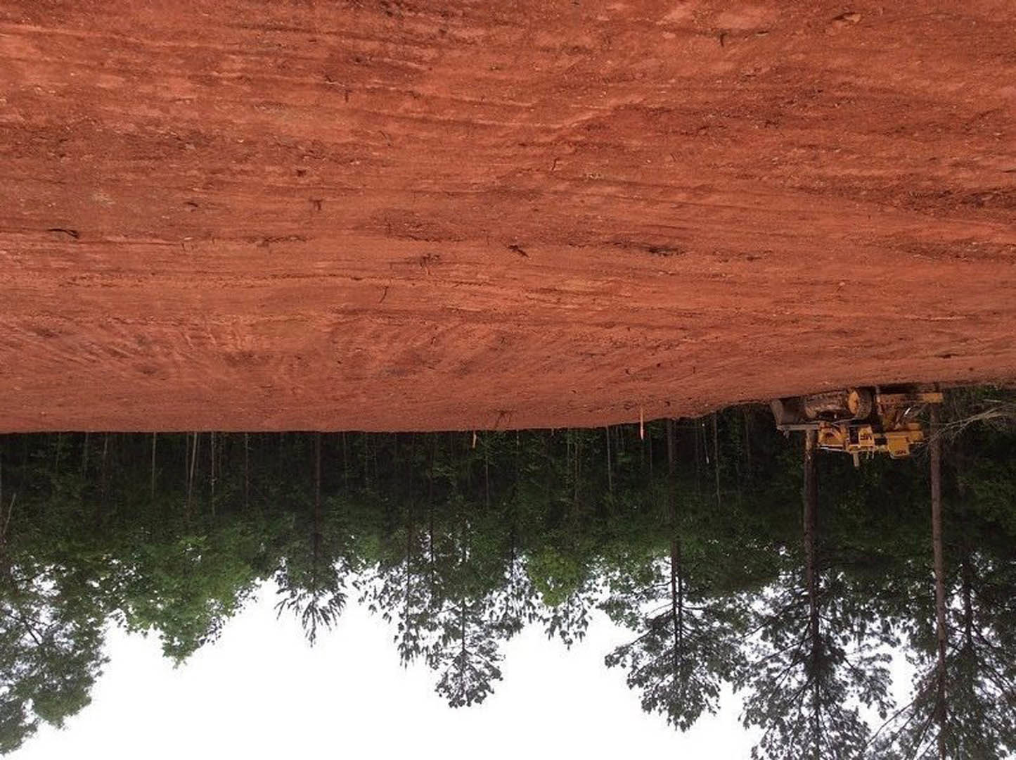 Tractor parked on a dirt road bordered by trees, with a lake reflecting surrounding nature in the background.