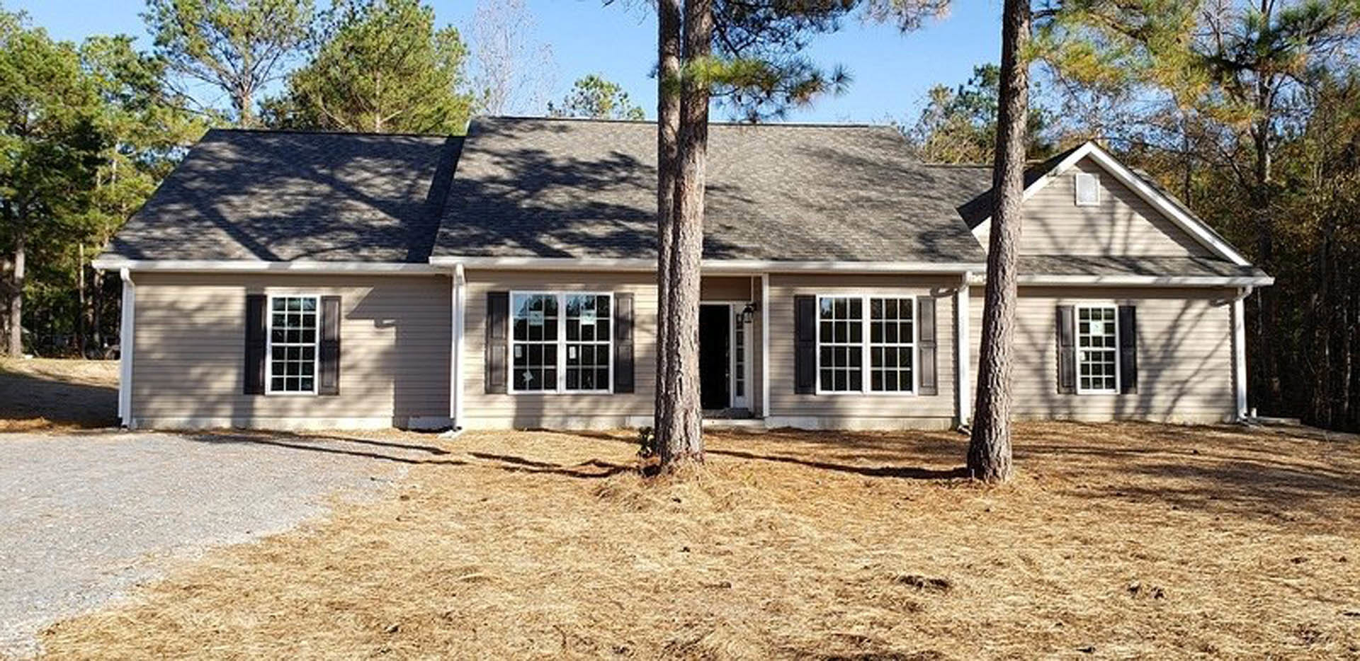 Two-story custom home with white siding, multiple-paned windows, and a gabled roof, surrounded by mature trees and landscaped front yard