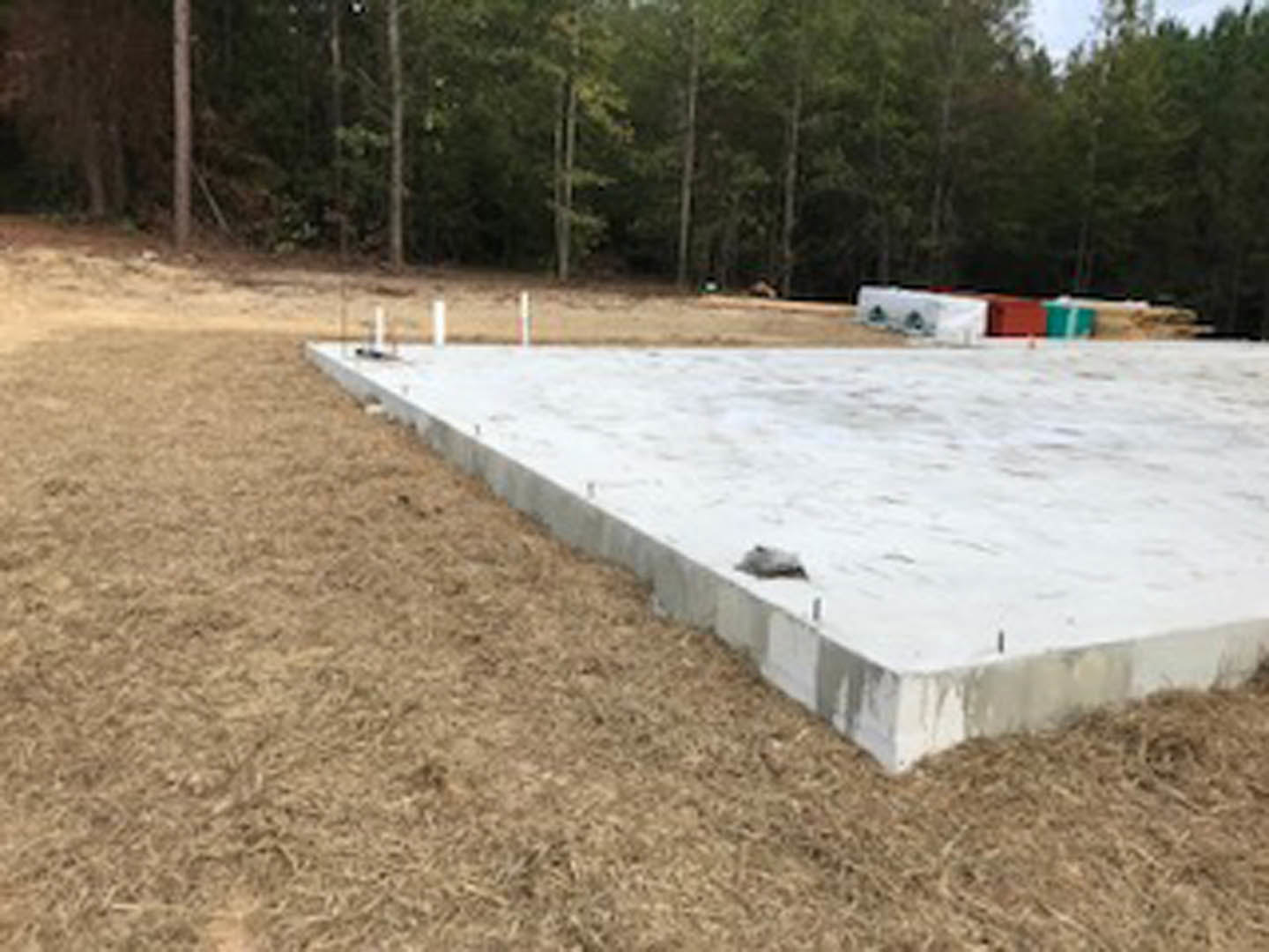 Concrete slab foundation set in grassy field with trees in background
