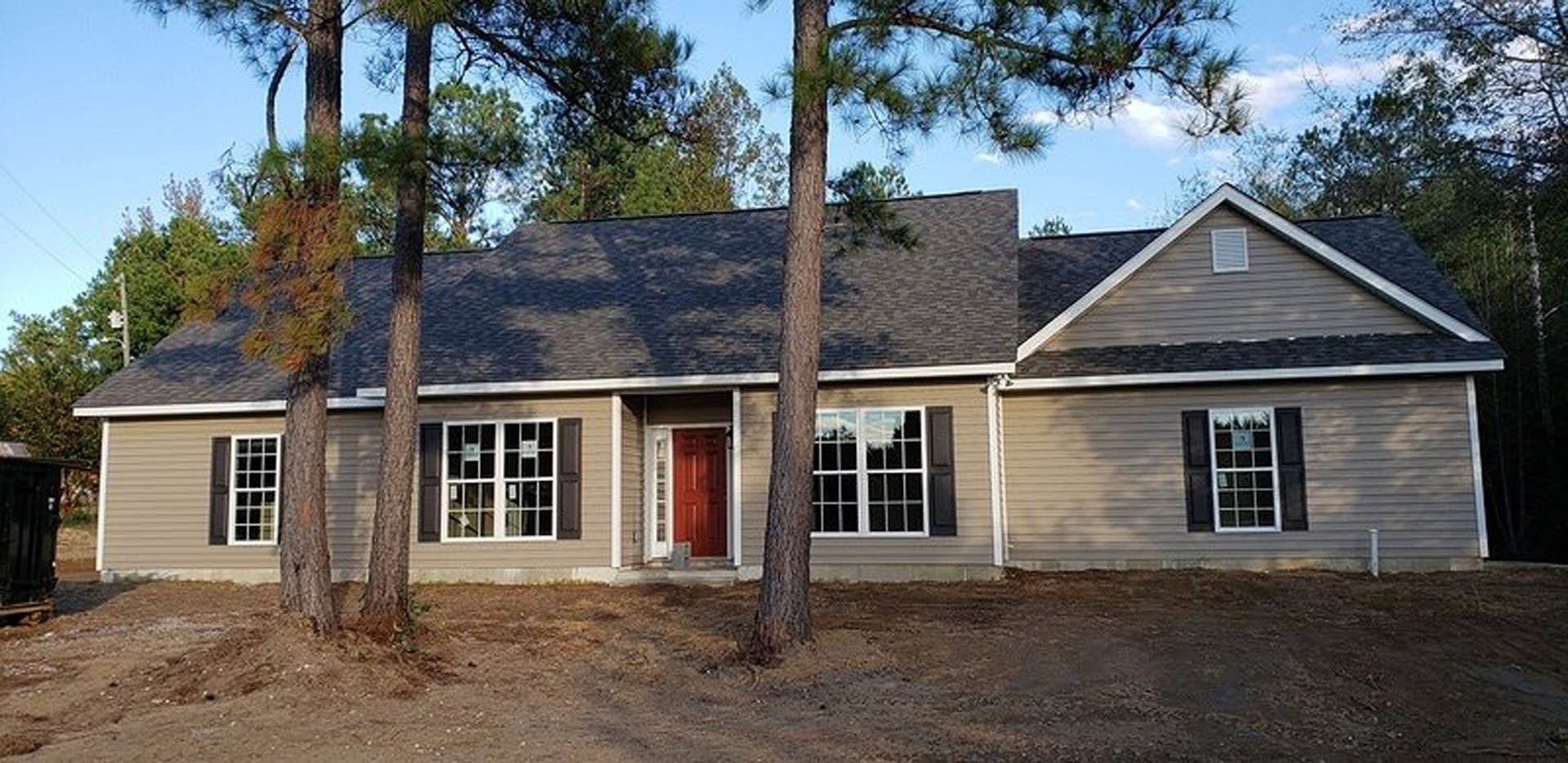 Two-story house with light siding, black shuttered windows, white window frames, red front door, and mature trees in landscaped front yard