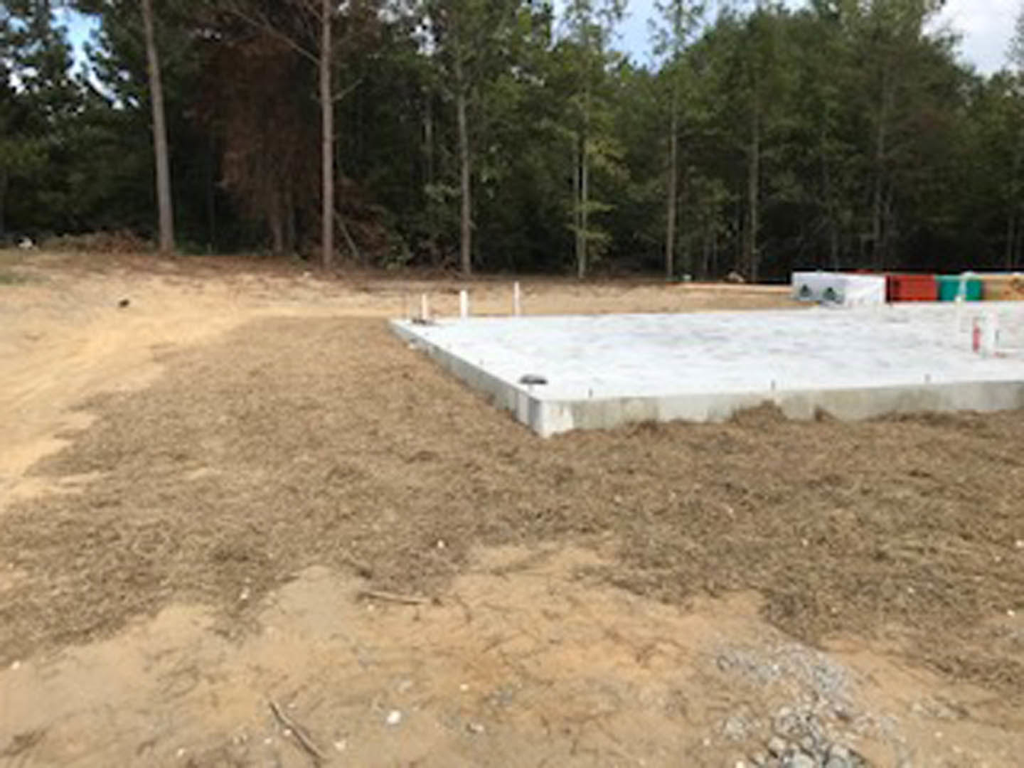 Concrete foundation slab set in a dirt field with scattered trees and blue sky in the background