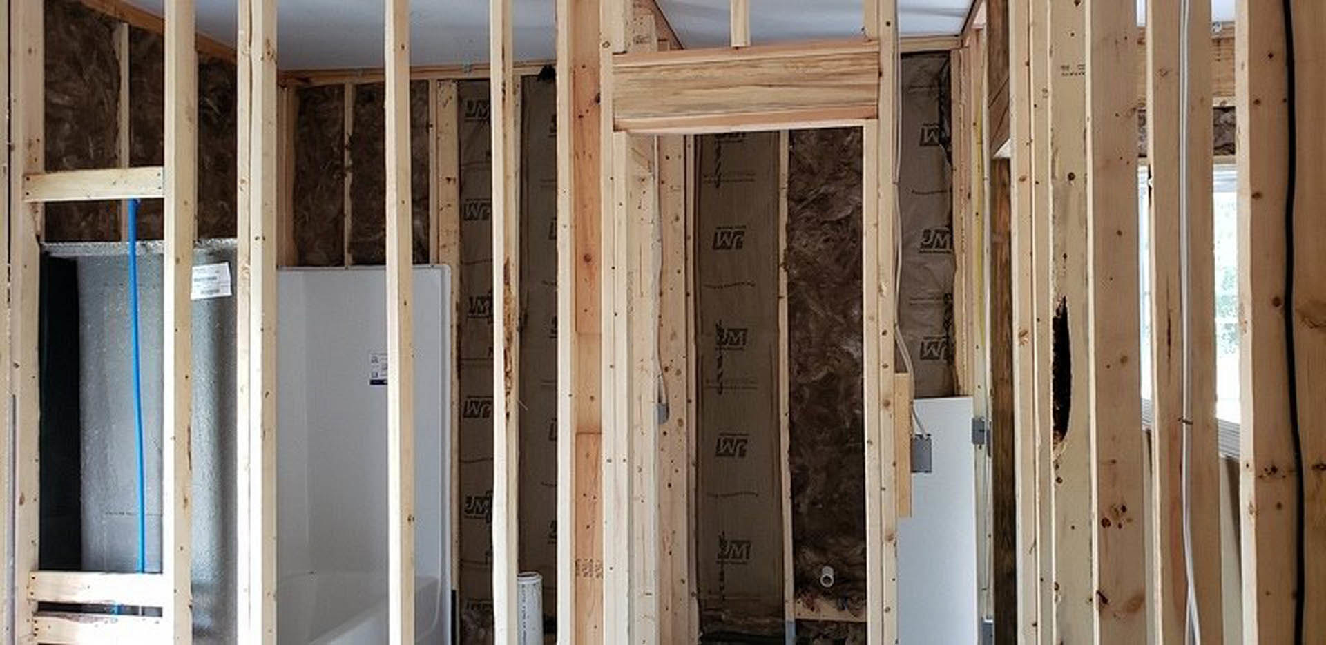 Bathroom under construction with exposed wood framing, installed bathtub, unfinished shower area, and construction materials scattered throughout