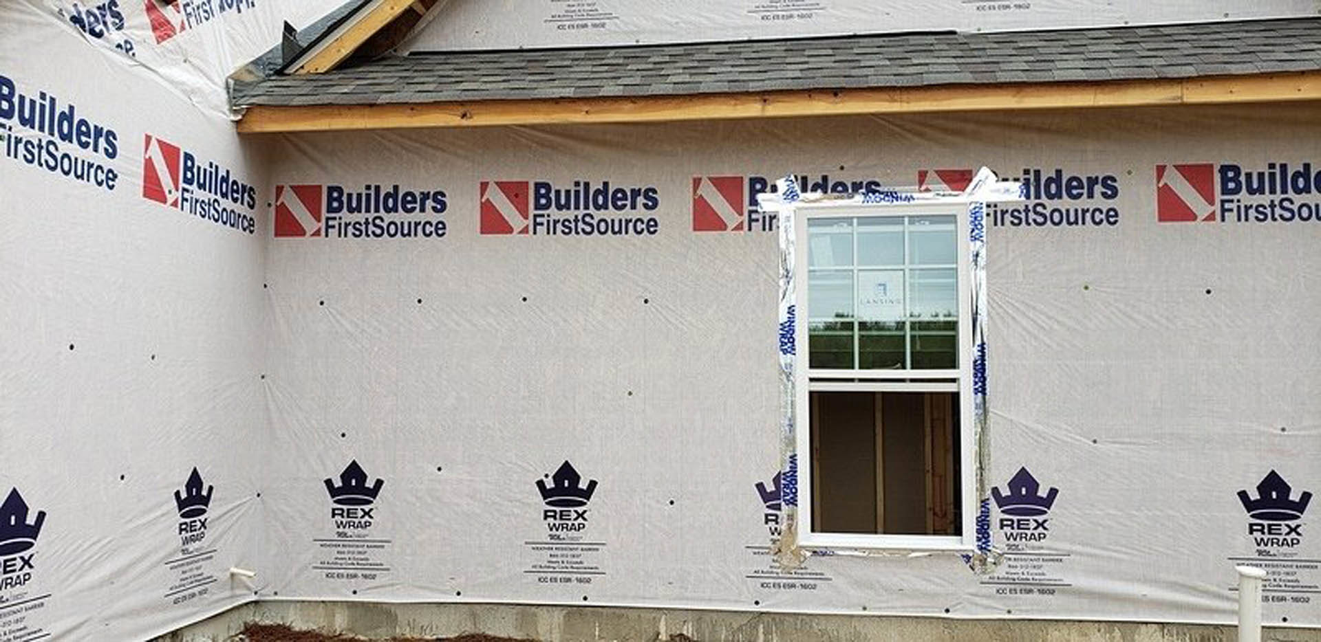 Framed exterior wall with exposed wood studs and a single installed window, construction materials visible on site