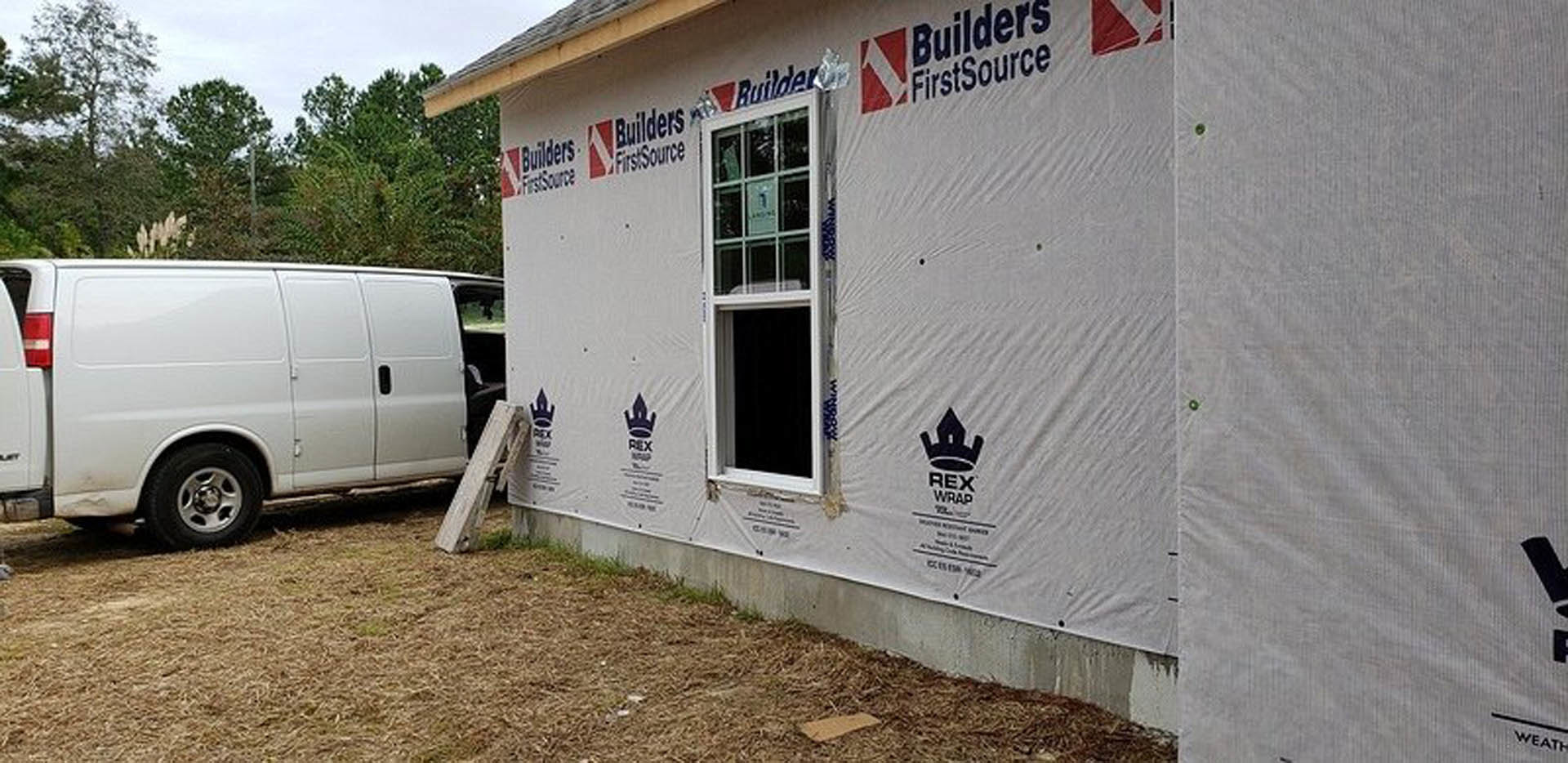 White van parked beside modern house with gray siding, large windows, and surrounding trees