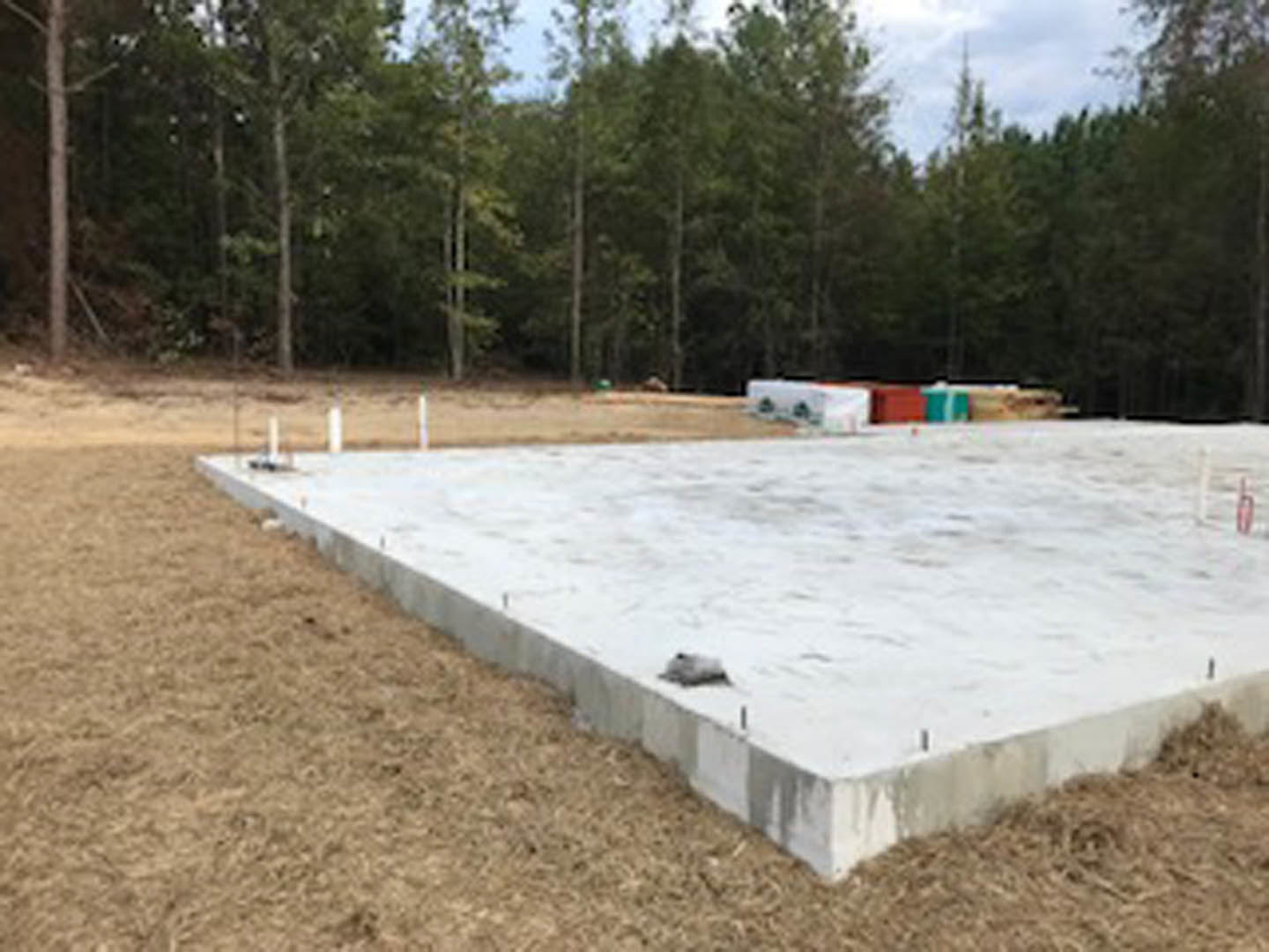 Concrete foundation slab set in grassy field with mature trees and blue sky in background
