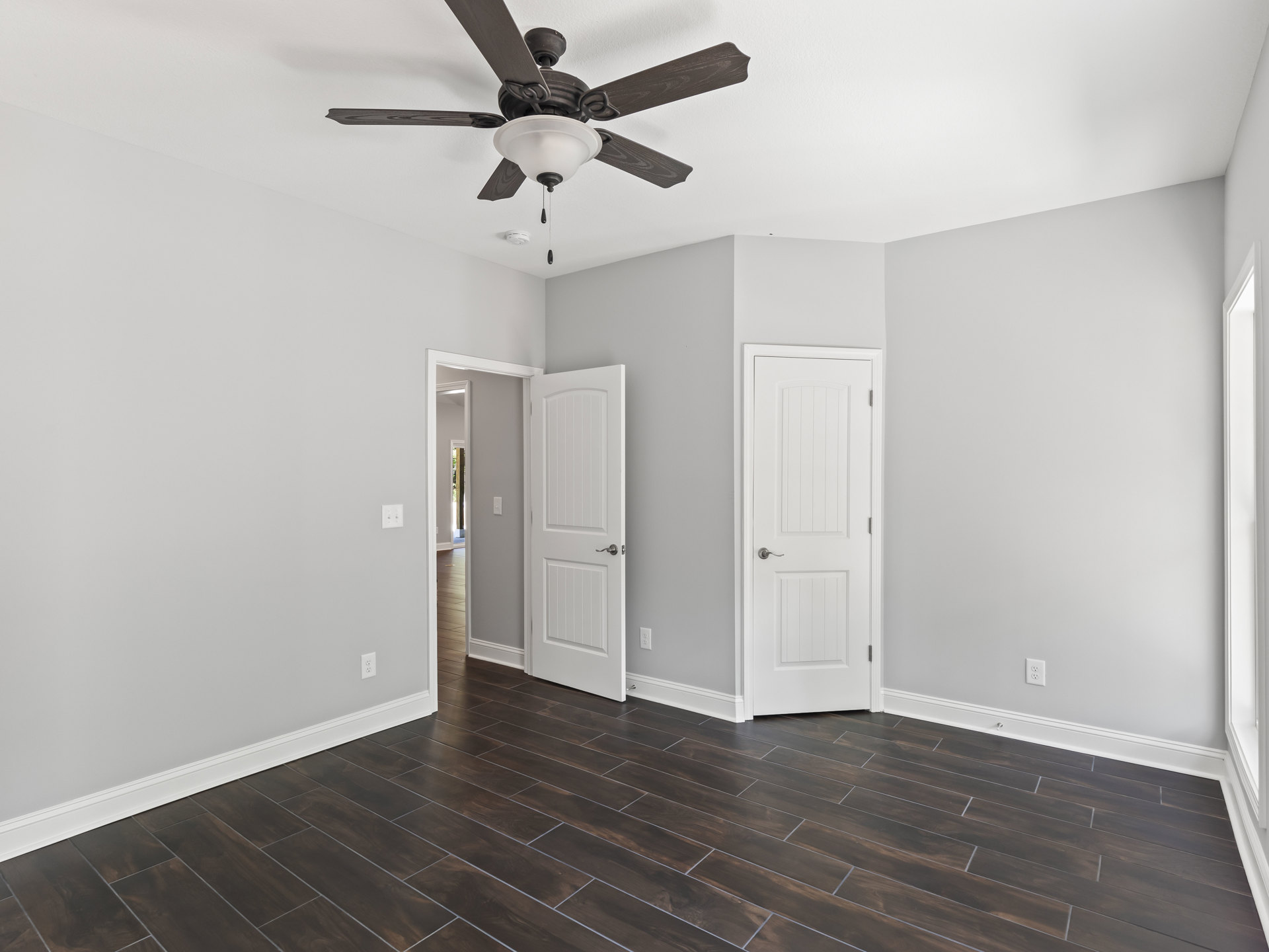 Ceiling fan with light fixture mounted on white plaster ceiling, wood flooring, white doors with silver handles, neutral walls