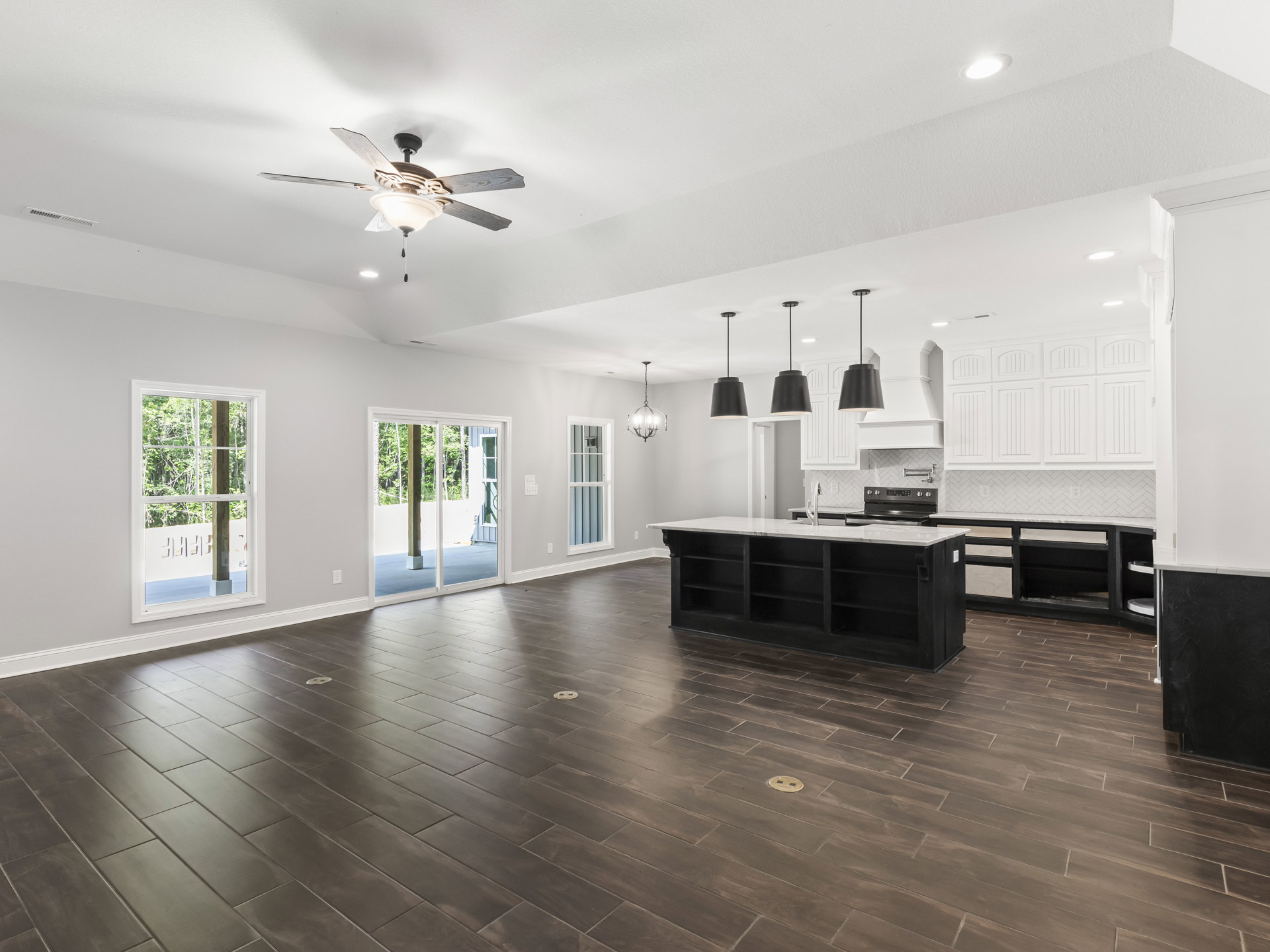Open-concept room featuring a black and white kitchen counter, hardwood floors, ceiling fan with light fixture, piano at center, window overlooking trees, and black ceiling lamp