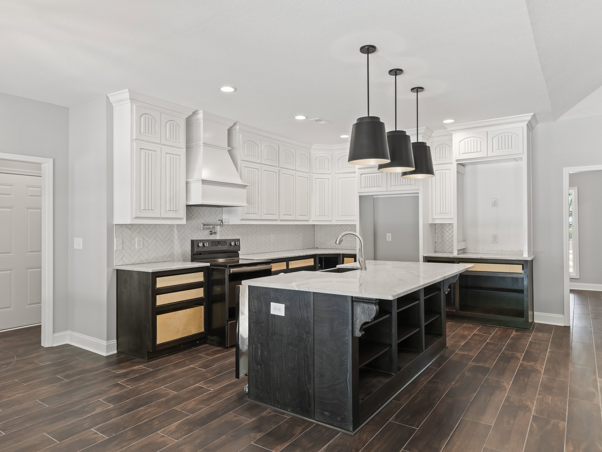 White kitchen cabinets and black appliances, kitchen island with sink, black and white countertop, black light fixture, white door with white frame, black wood cabinet with white
